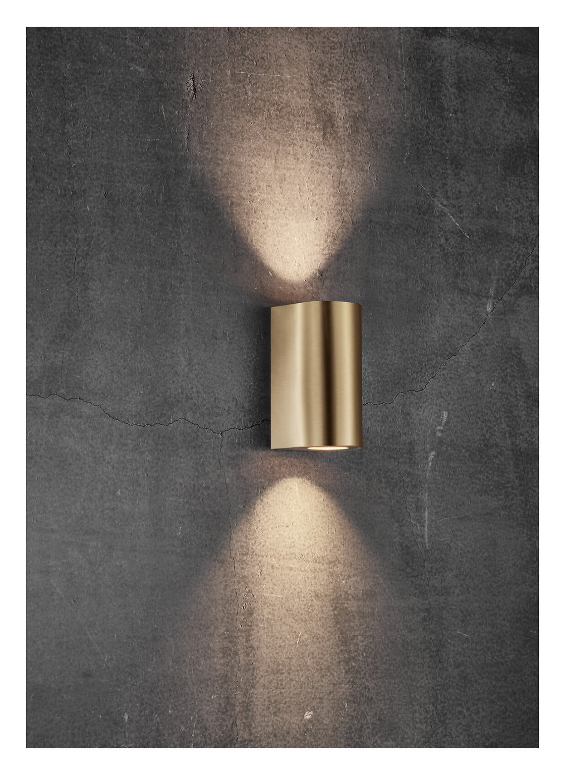 Eine goldene Wandleuchte ist an einer dunkelgrauen Wand montiert. Die Lampe strahlt Licht nach oben und unten und erzeugt einen Spot-Effekt.