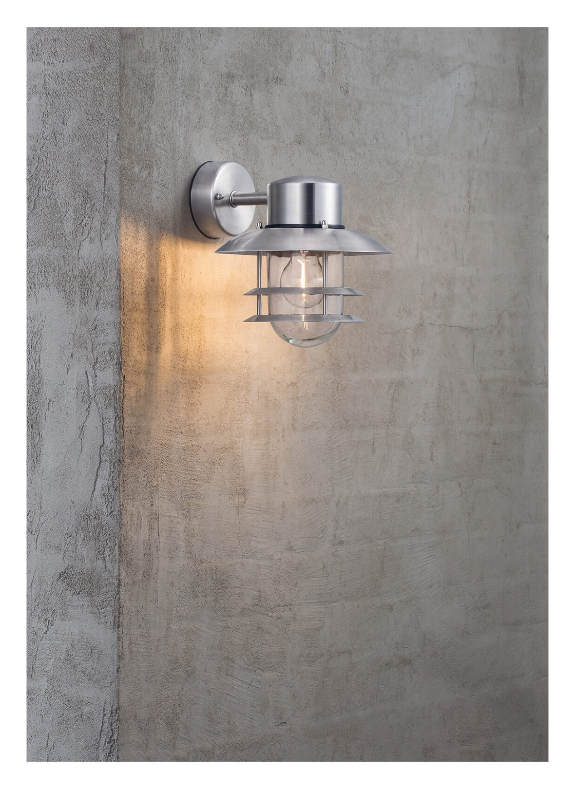 Eine Metall-Wandleuchte mit Glasgehäuse und Glühbirne ist an einer strukturierten grauen Betonwand angebracht.