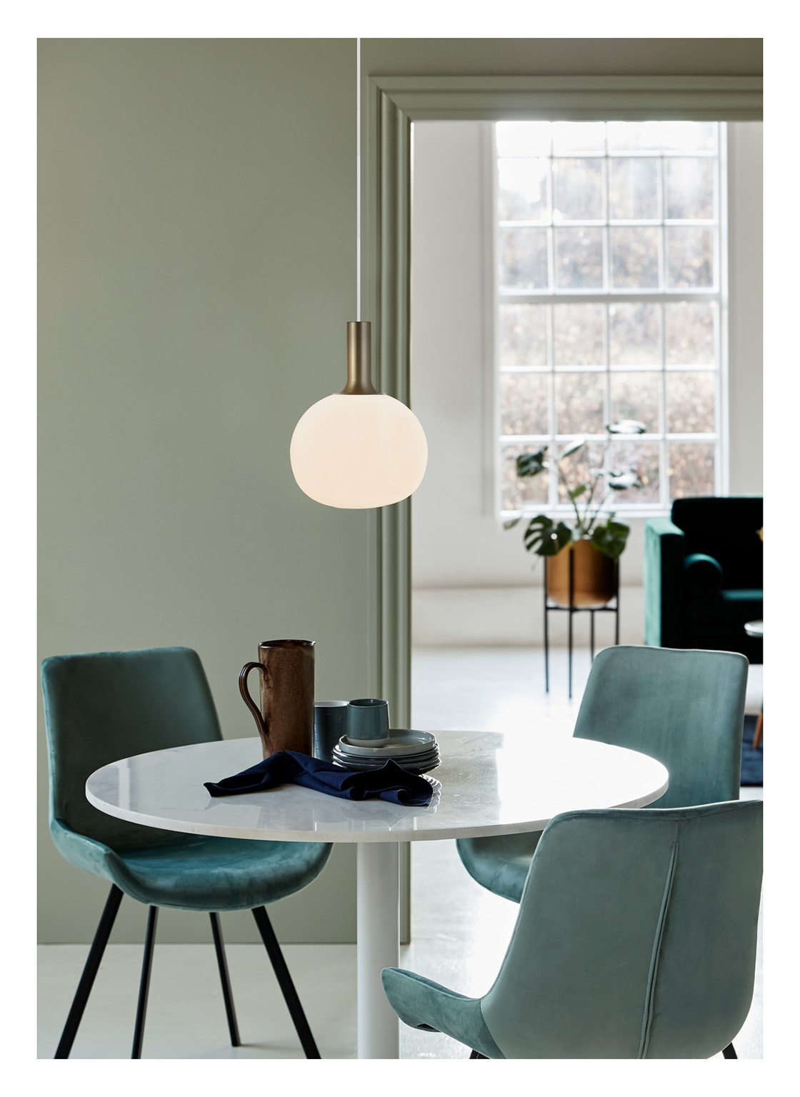 Une salle à manger avec une table blanche, des chaises turquoise, une suspension et une fenêtre en arrière-plan.