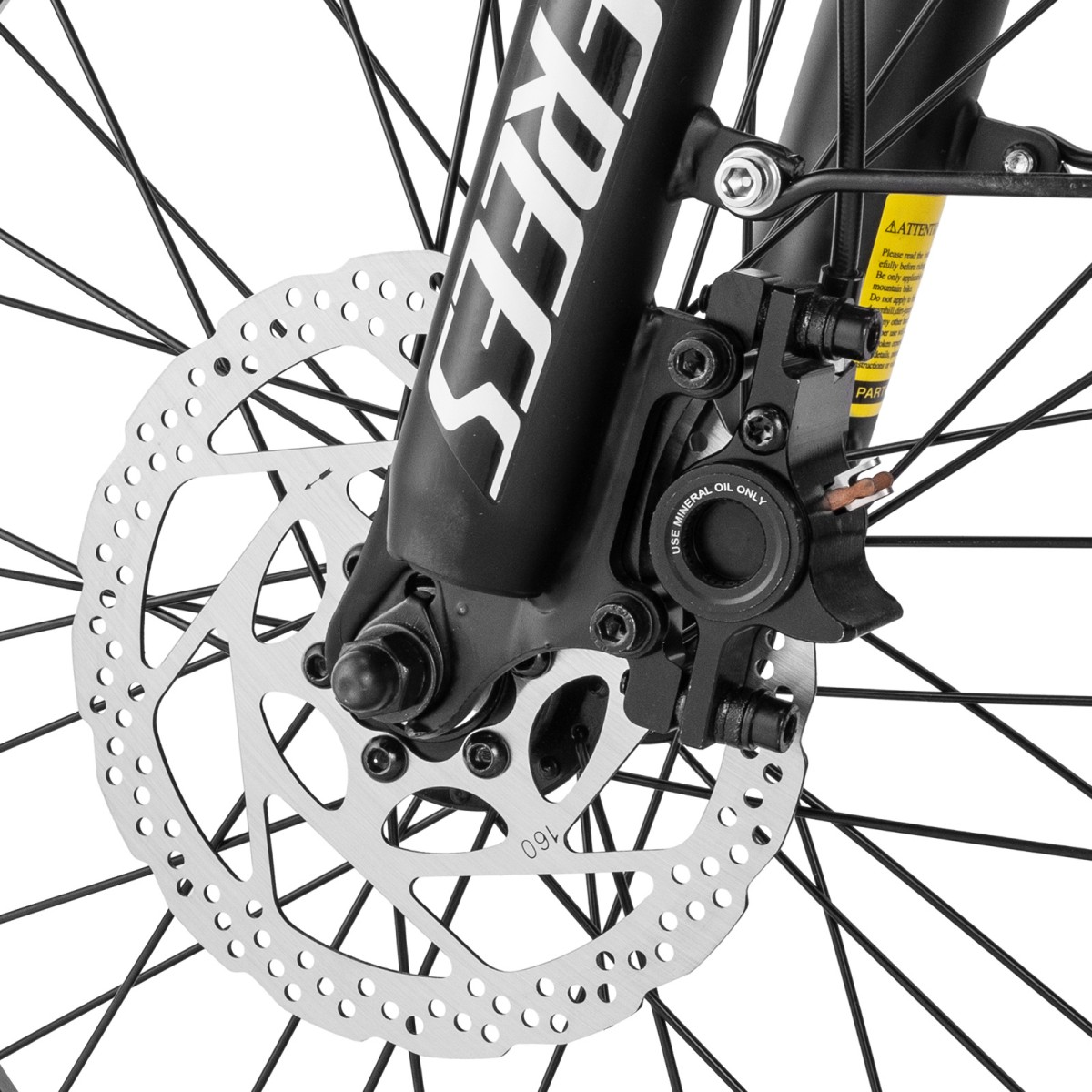 Zbliżenie przedniego koła roweru. Srebrny hamulec tarczowy z otworami, czarna rama, szprychy i żółta etykieta ostrzegawcza są widoczne.