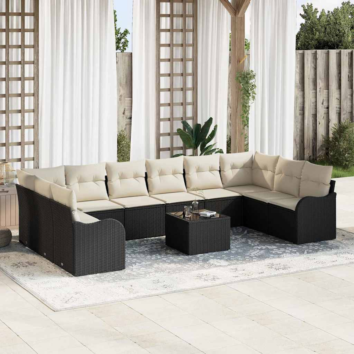 Ein Outdoor-Terrassenset mit schwarzen Korbmöbeln und cremefarbenen Kissen. Ein kleiner quadratischer Tisch steht in der Mitte auf einem gemusterten Teppich.