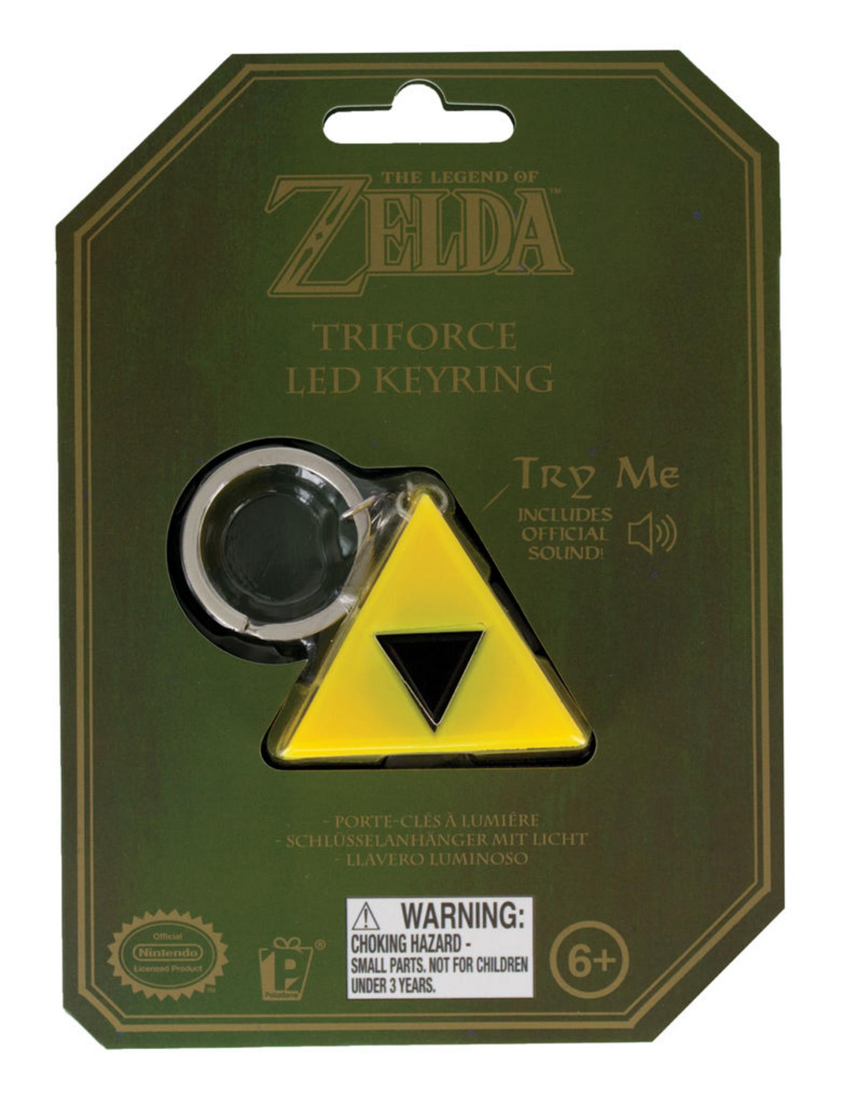 Ein Zelda Triforce LED-Schlüsselanhänger auf einer grünen Karte. Das Triforce ist gelb mit einem schwarzen Dreieck. Die Karte hat Text und Warnhinweise.