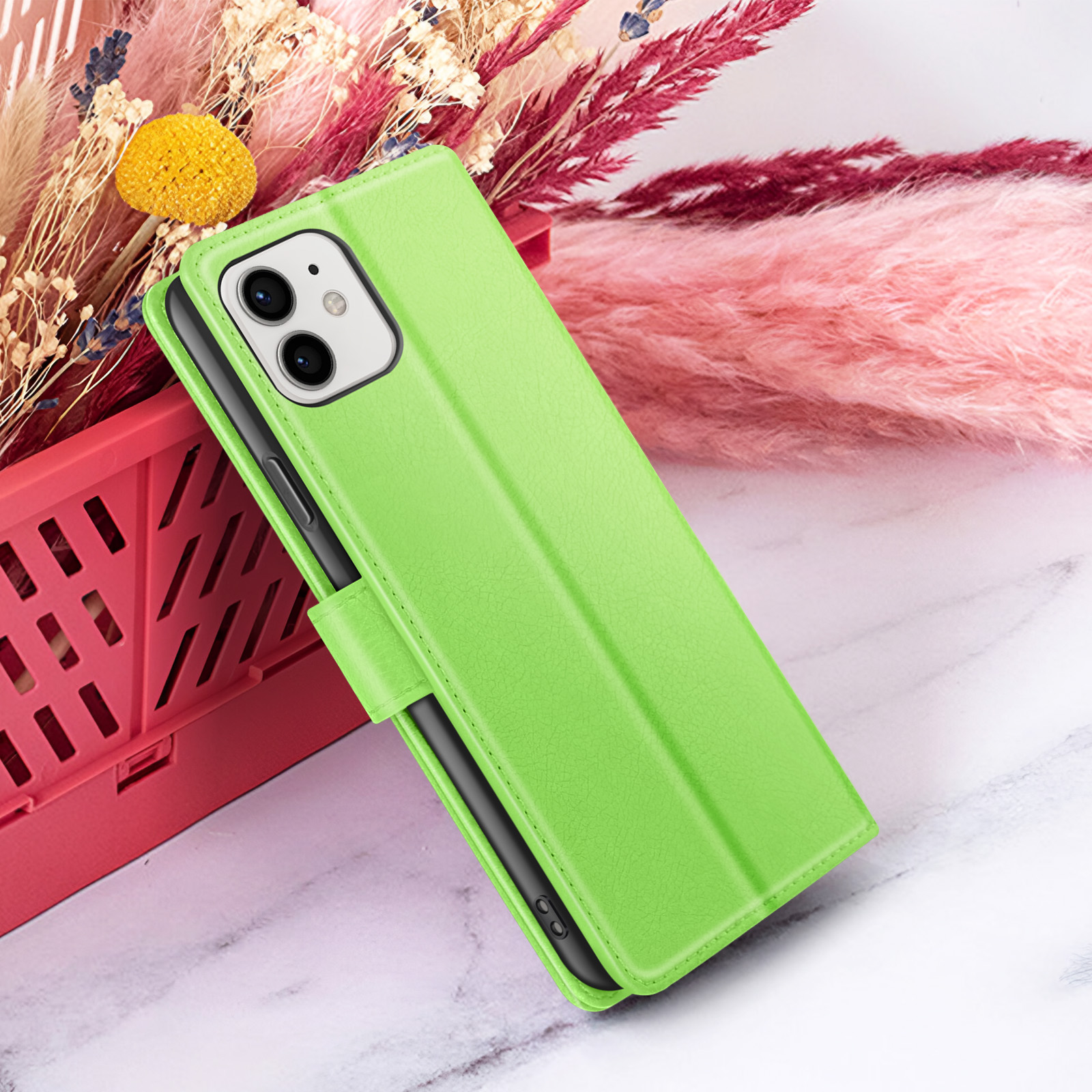 Un étui de téléphone vert avec un téléphone est affiché sur une surface en marbre, avec des fleurs séchées en arrière-plan.