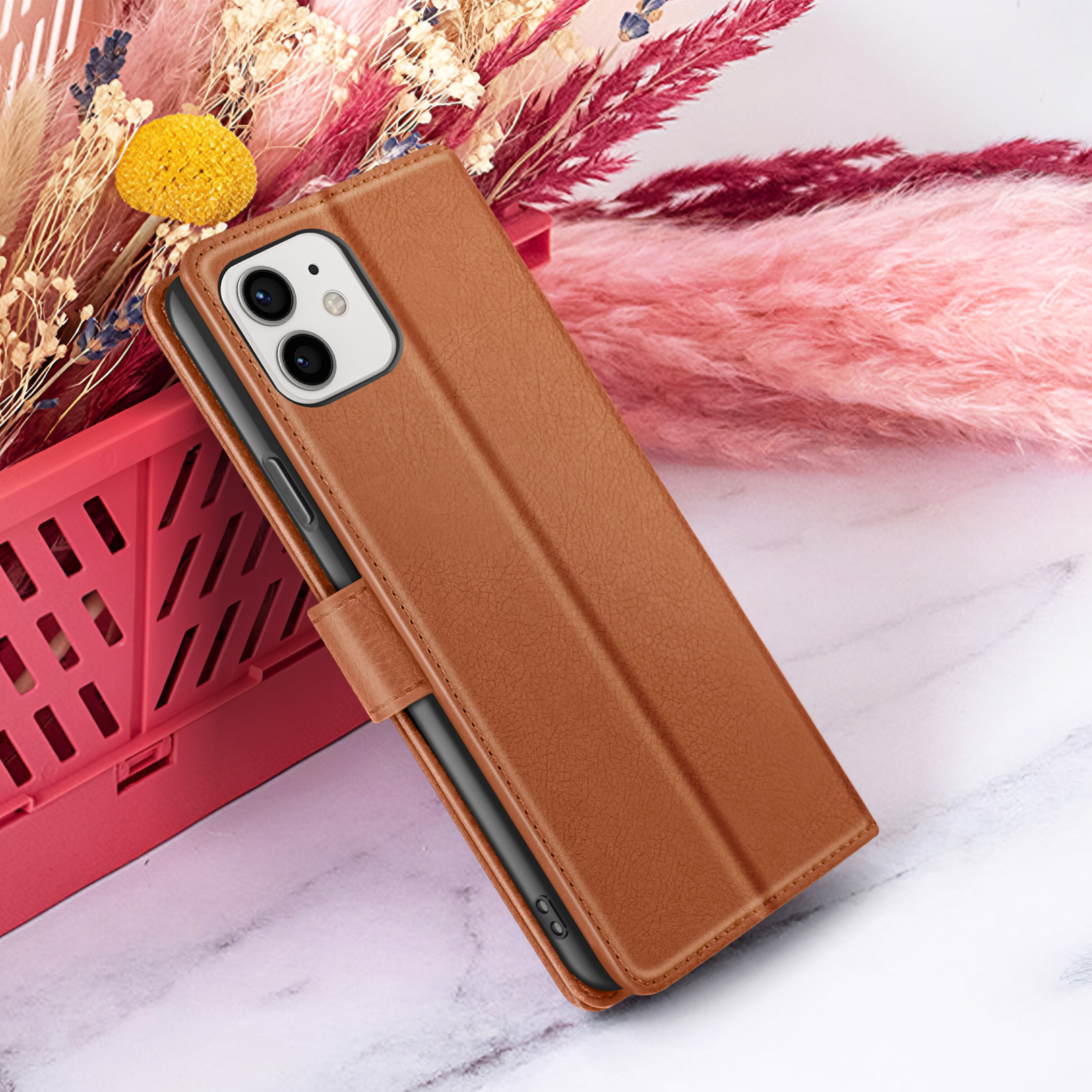 Bruine leren telefoonhoes met telefoon erin. Achtergrond: roze bloemen en een rode container. Wit en grijs marmeren oppervlak.