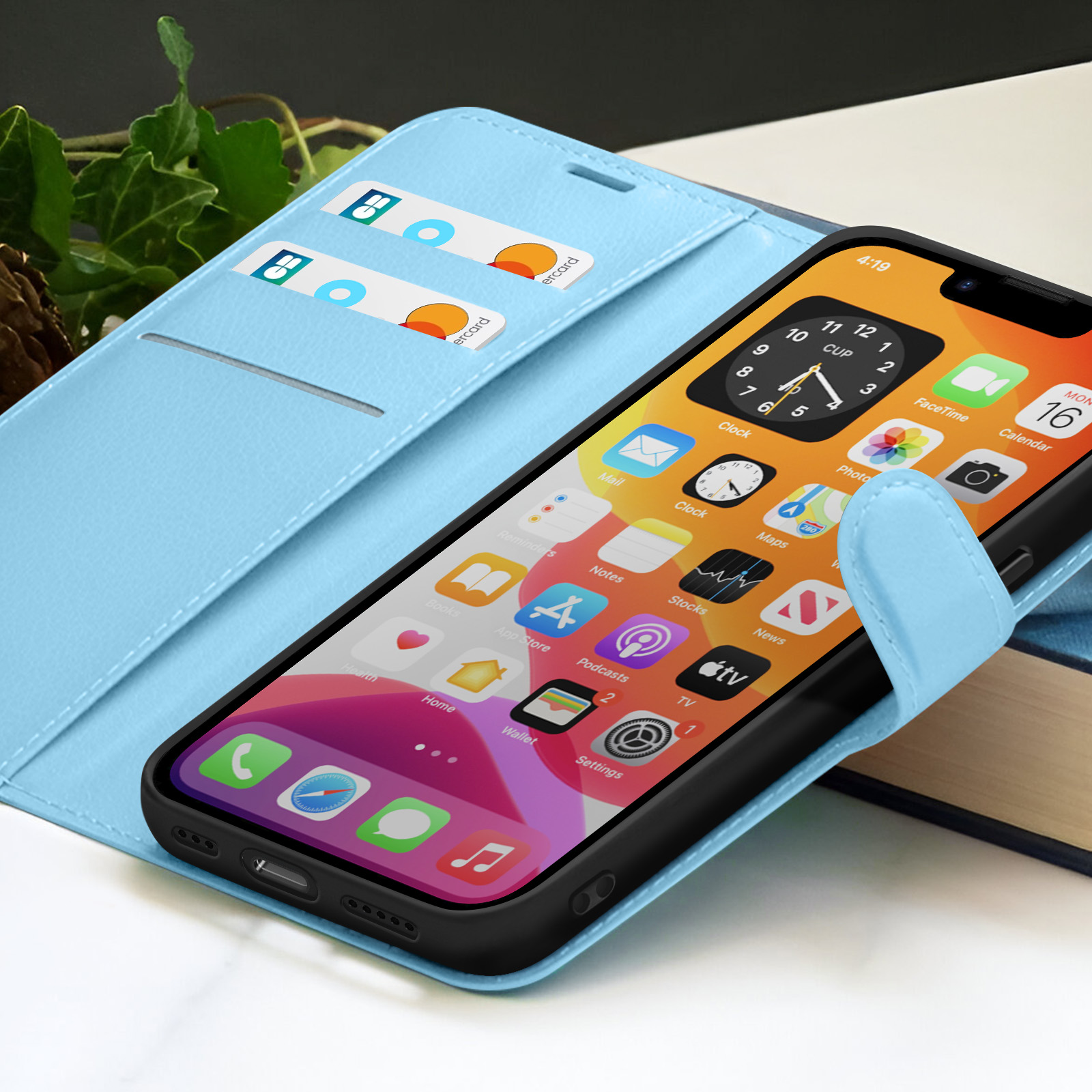 Een smartphone in een lichtblauwe hoes met kaarten. Het scherm toont app-pictogrammen. Op de achtergrond is een boek zichtbaar.