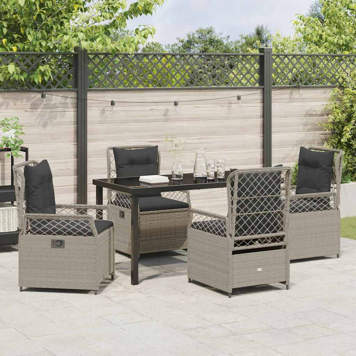 Terrassengarnitur mit Tisch und vier Stühlen. Die Stühle haben schwarze Kissen. Im Hintergrund befinden sich ein Zaun und Bäume.