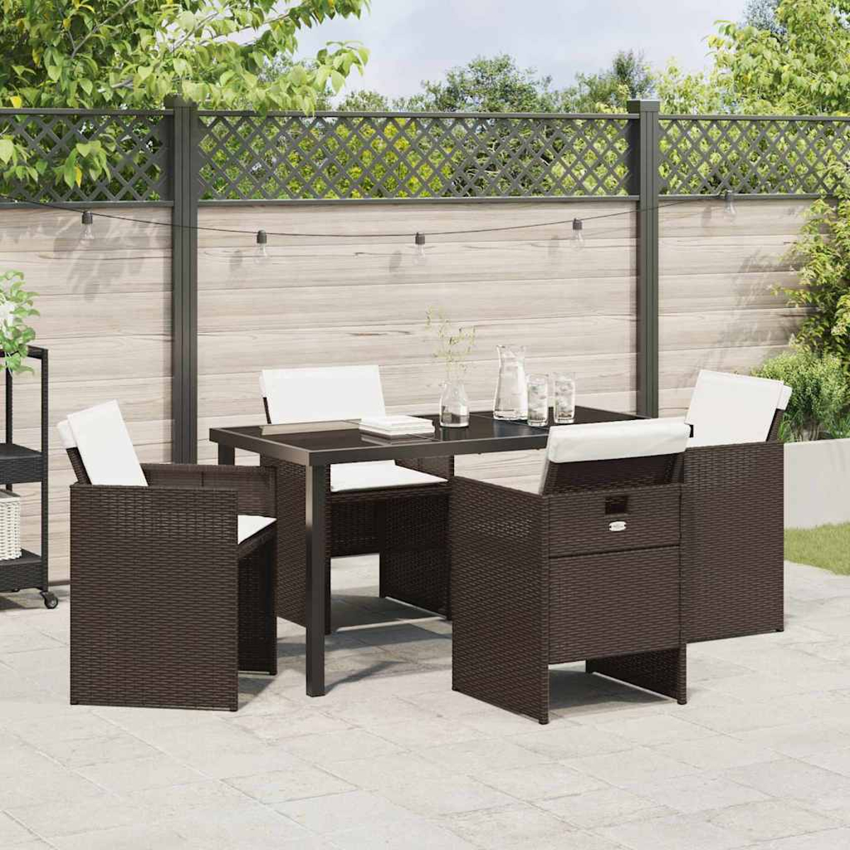 Set da patio esterno con tavolo e sedie scure. Cuscini bianchi. Sfondo con recinzione in legno e luci a corda.