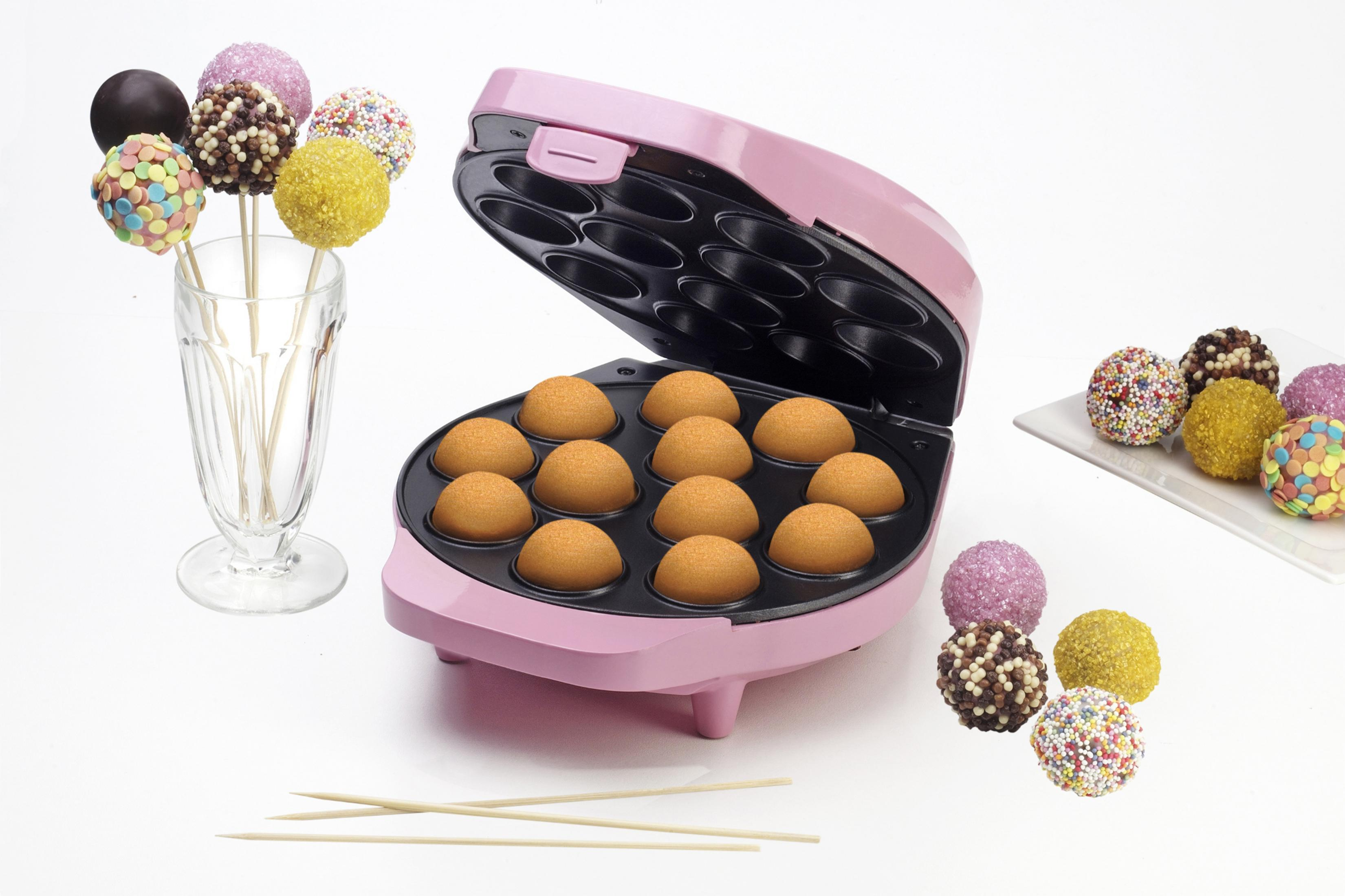 Una máquina rosa para hacer cake pops con cake pops dentro y a un lado, con un vaso de cake pops en palitos.