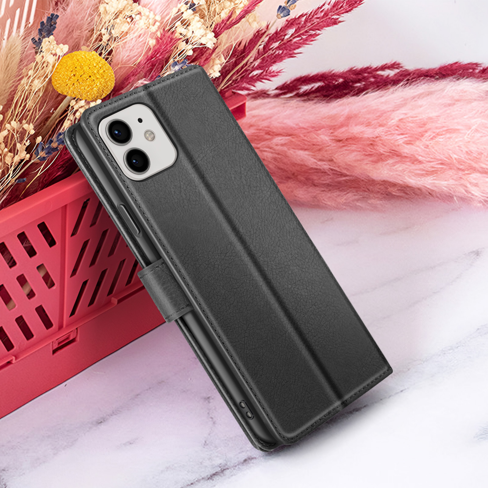 Een zwarte telefoonhoes, met een telefoon erin, ligt op een marmeren oppervlak. Roze en beige bloemen op de achtergrond.