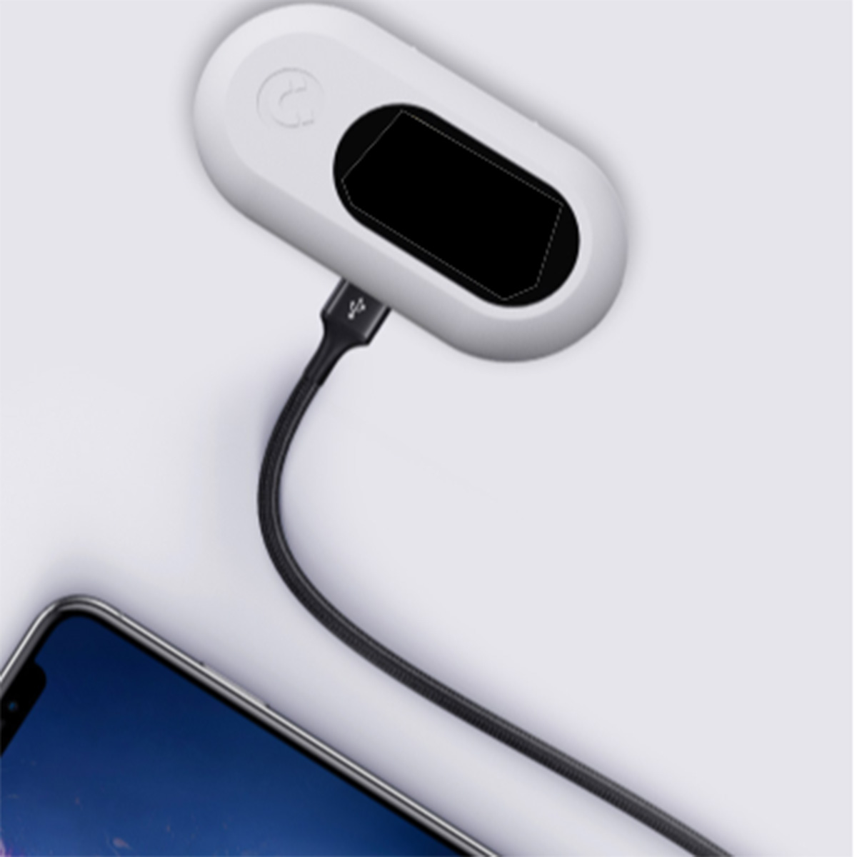 Ein weißes, ovales Gerät mit schwarzem Bildschirm ist über ein schwarzes Kabel mit einem Telefon verbunden. Das Telefon hat einen blauen Bildschirm.