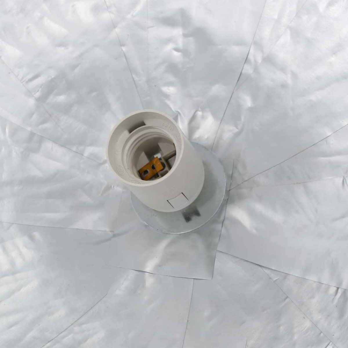 Eine weiße Glühbirnenfassung auf einem Metallsockel, umgeben von zerknittertem, reflektierendem Silbermaterial.