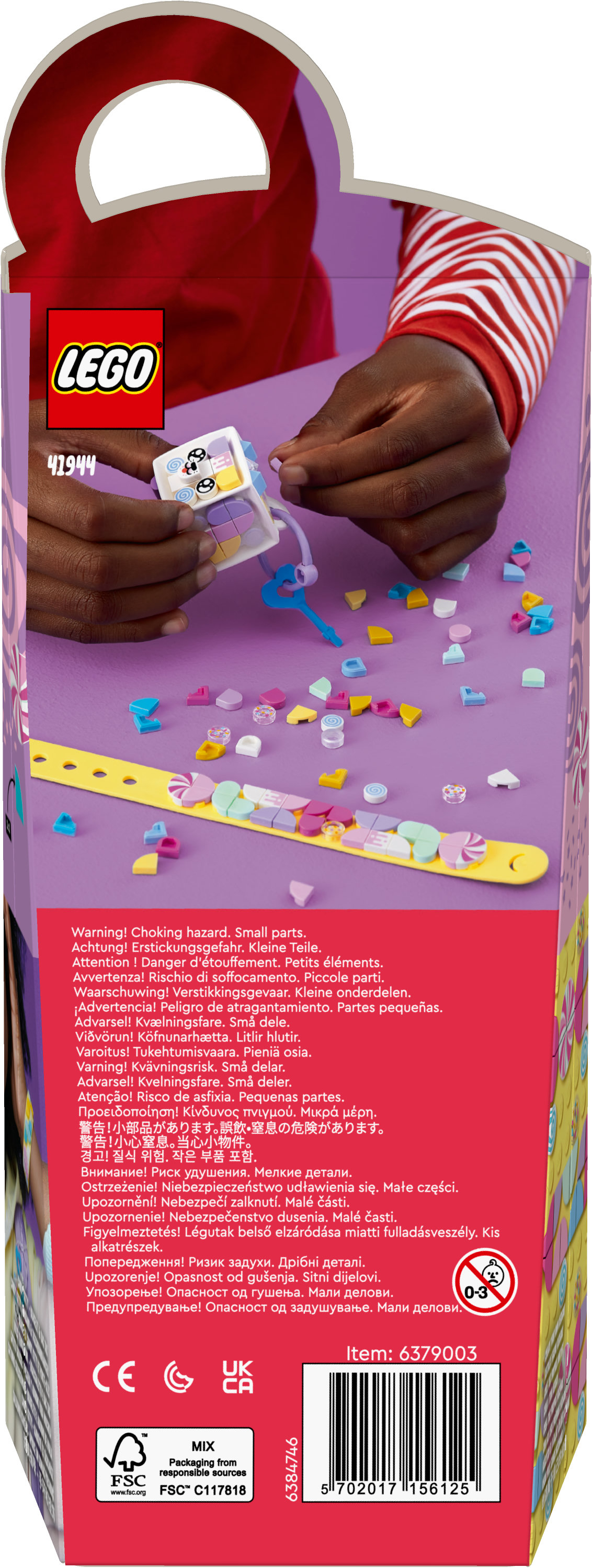 Eine LEGO-Box zeigt Kinderhände, die einen Würfel halten. Der Würfel hat bunte Dekorationen, und es gibt verstreute Kleinteile.