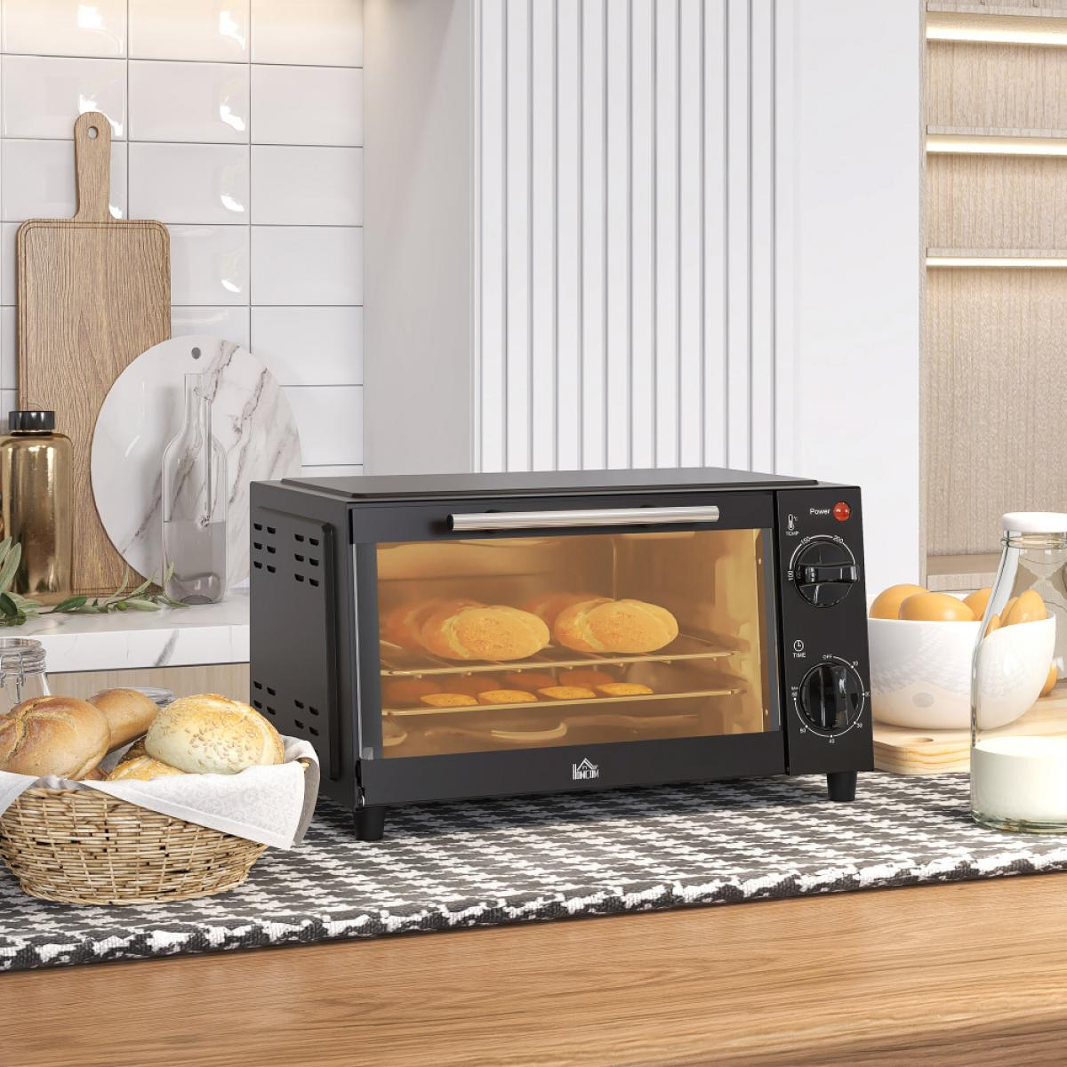 Ein schwarzer Toaster mit gebackenem Brot darin. Vorne steht ein Brotkorb. Küchenhintergrund mit Schneidebrettern und Fliesen.
