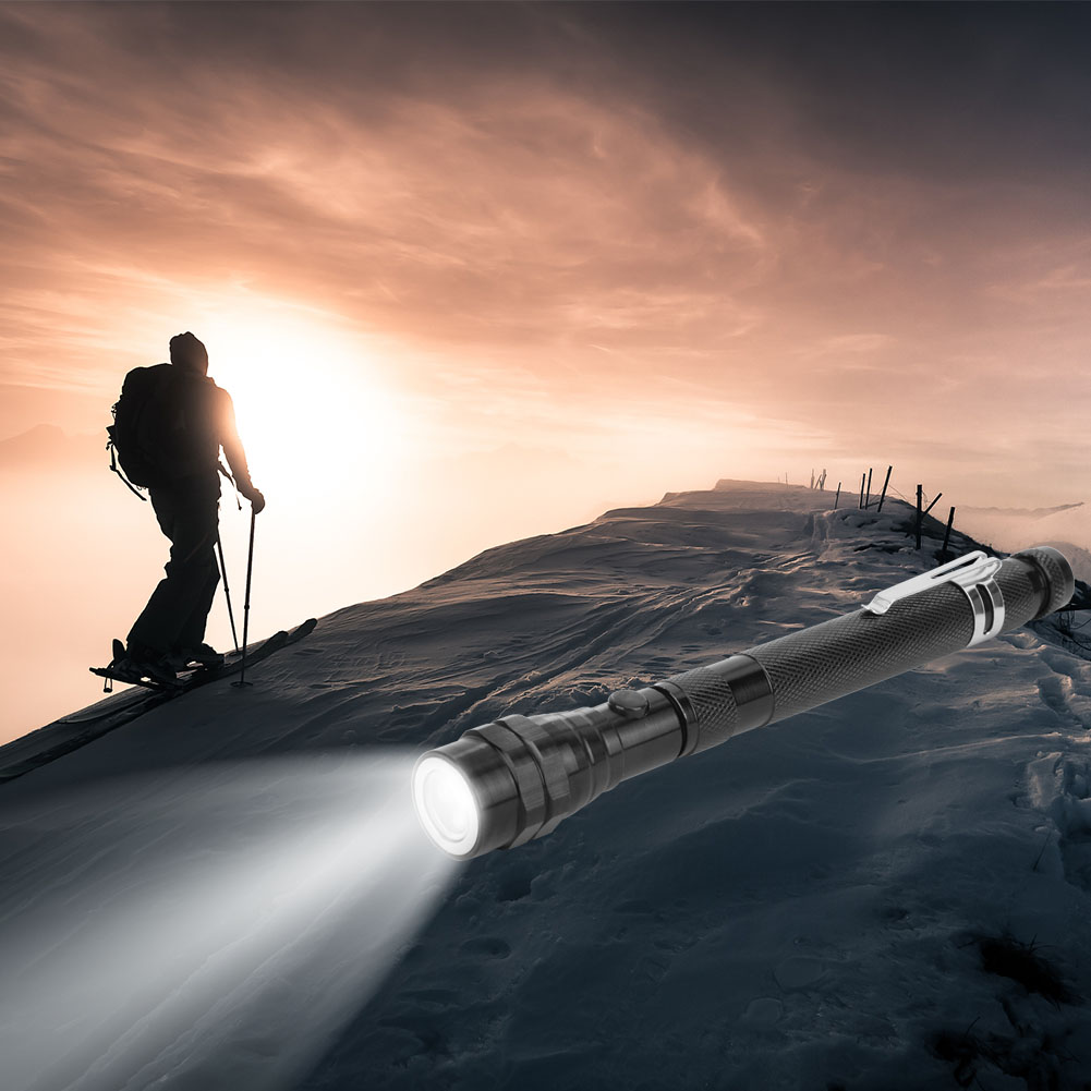 Eine Taschenlampe beleuchtet einen verschneiten Bergpfad. Im Hintergrund steigt ein Skifahrer auf. Der Himmel ist orange und rosa.