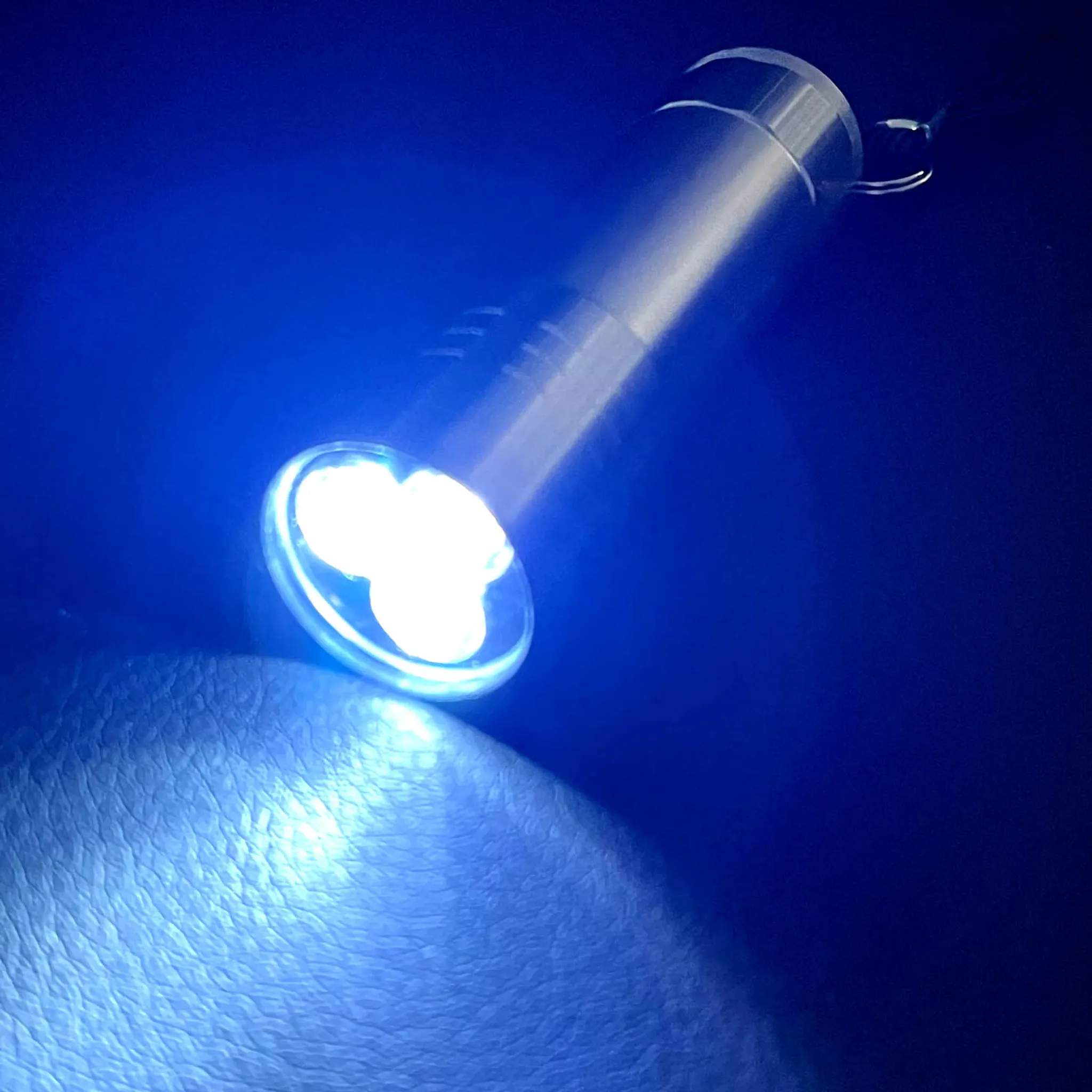 Eine silberne Taschenlampe strahlt hellblaues Licht auf eine strukturierte Oberfläche, der Hintergrund ist dunkelblau.