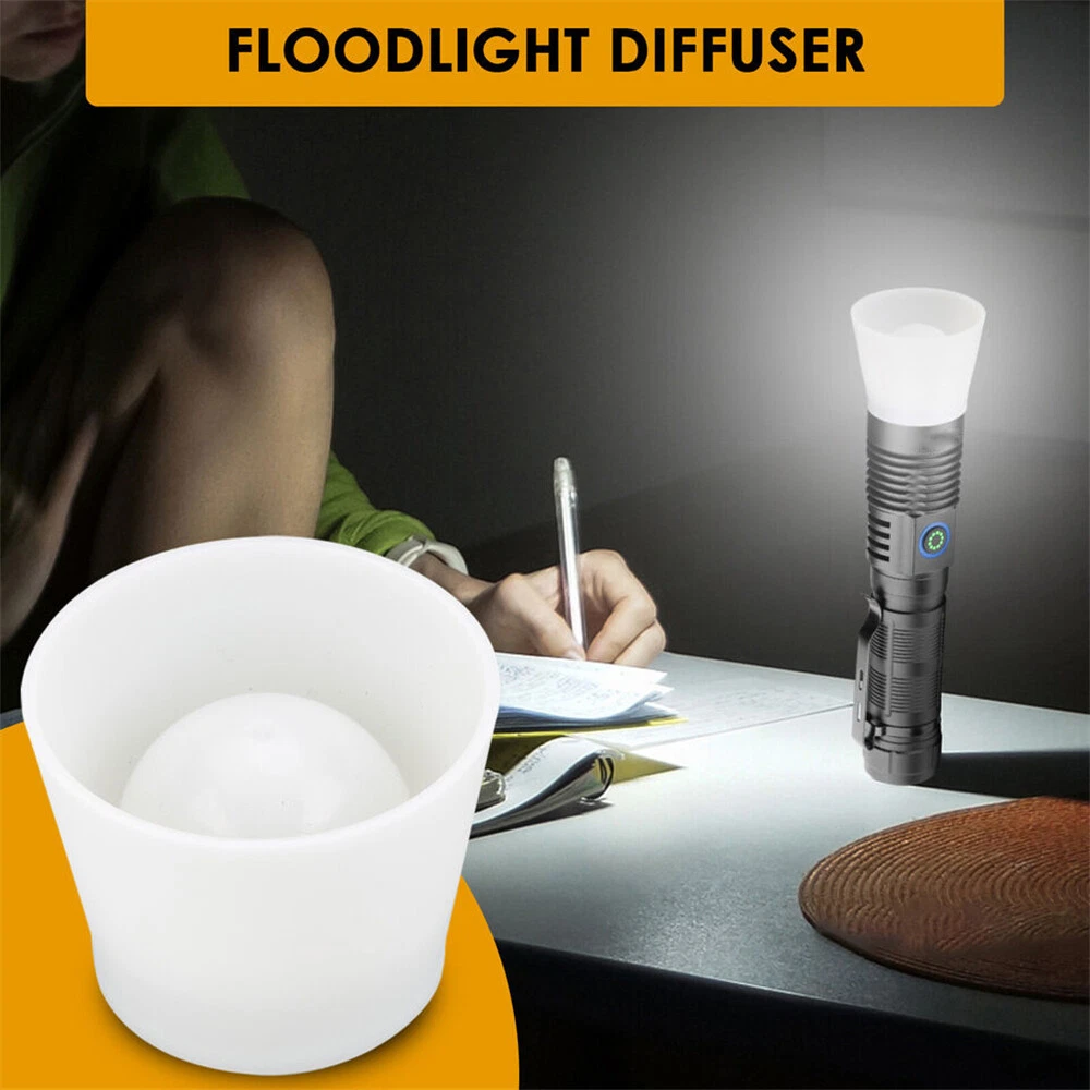 Ein weißer Flutlichtdiffusor und eine Taschenlampe stehen auf einem Tisch. Eine Person schreibt. Die Szene ist schwach beleuchtet.