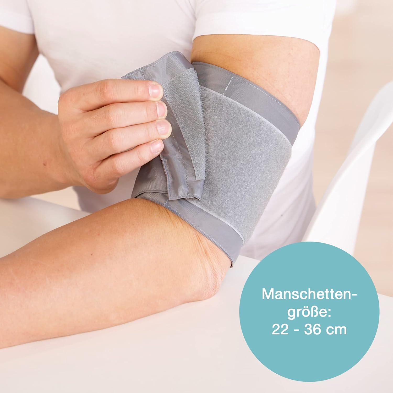 Eine Person trägt eine Blutdruckmanschette am Arm. Die Manschette ist grau, mit einem blauen Kreis mit Text zur Manschettengröße.