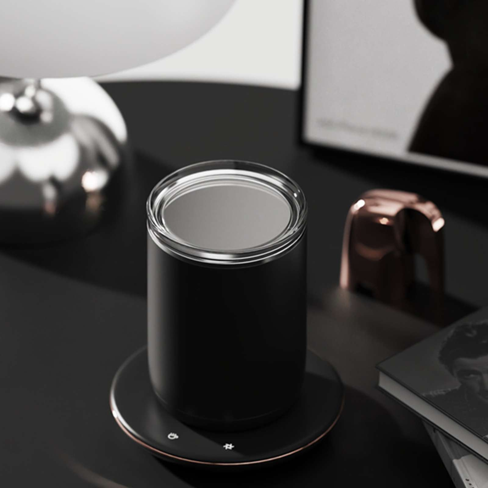 Ein schwarzer Kaffee wärmer mit einer Tasse darauf. Eine Elefantenfigur, ein Buch und eine Lampe sind ebenfalls vorhanden.