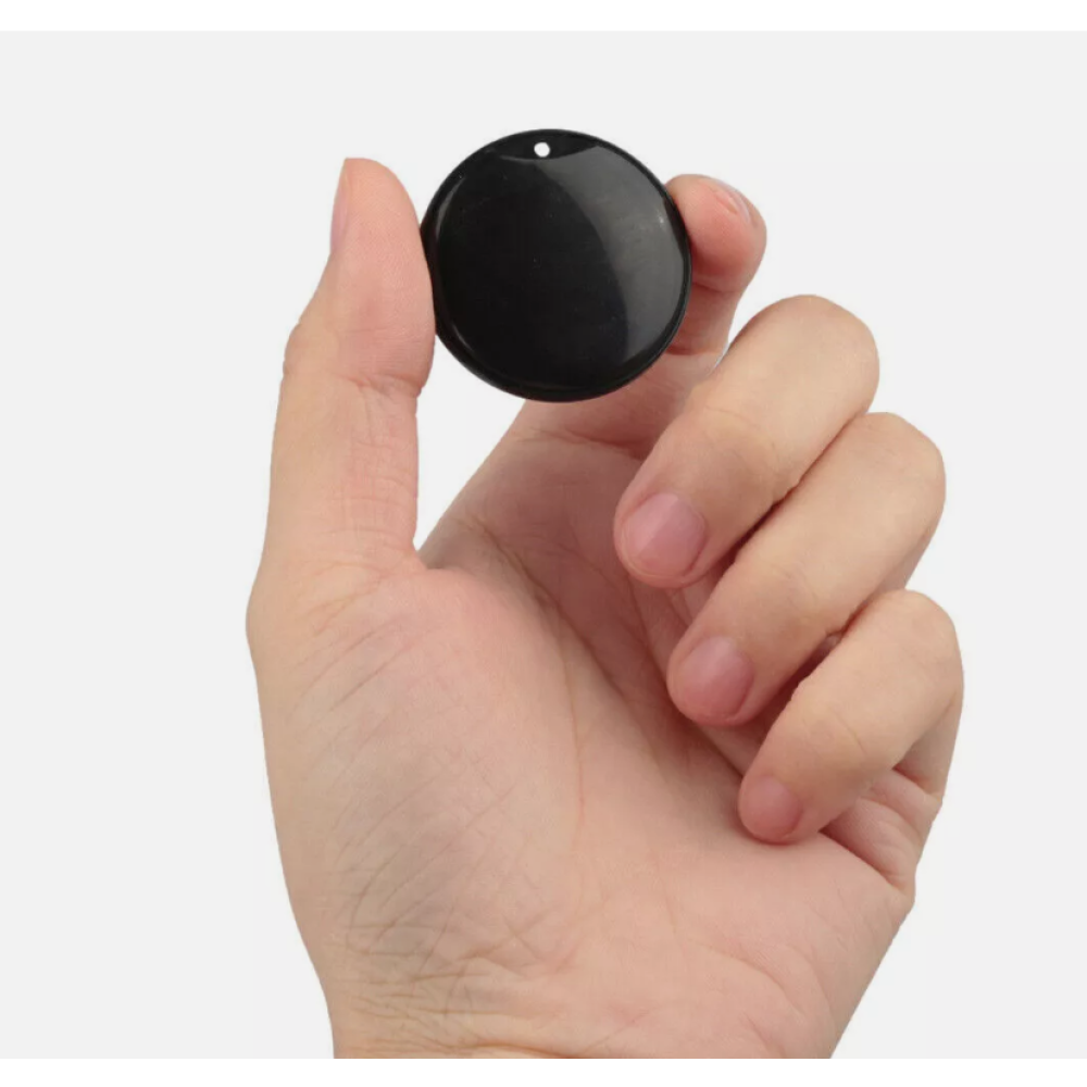 Eine Hand hält ein kleines, schwarzes, rundes Objekt. Das Objekt hat oben ein Loch. Der Hintergrund ist einfarbig weiß.