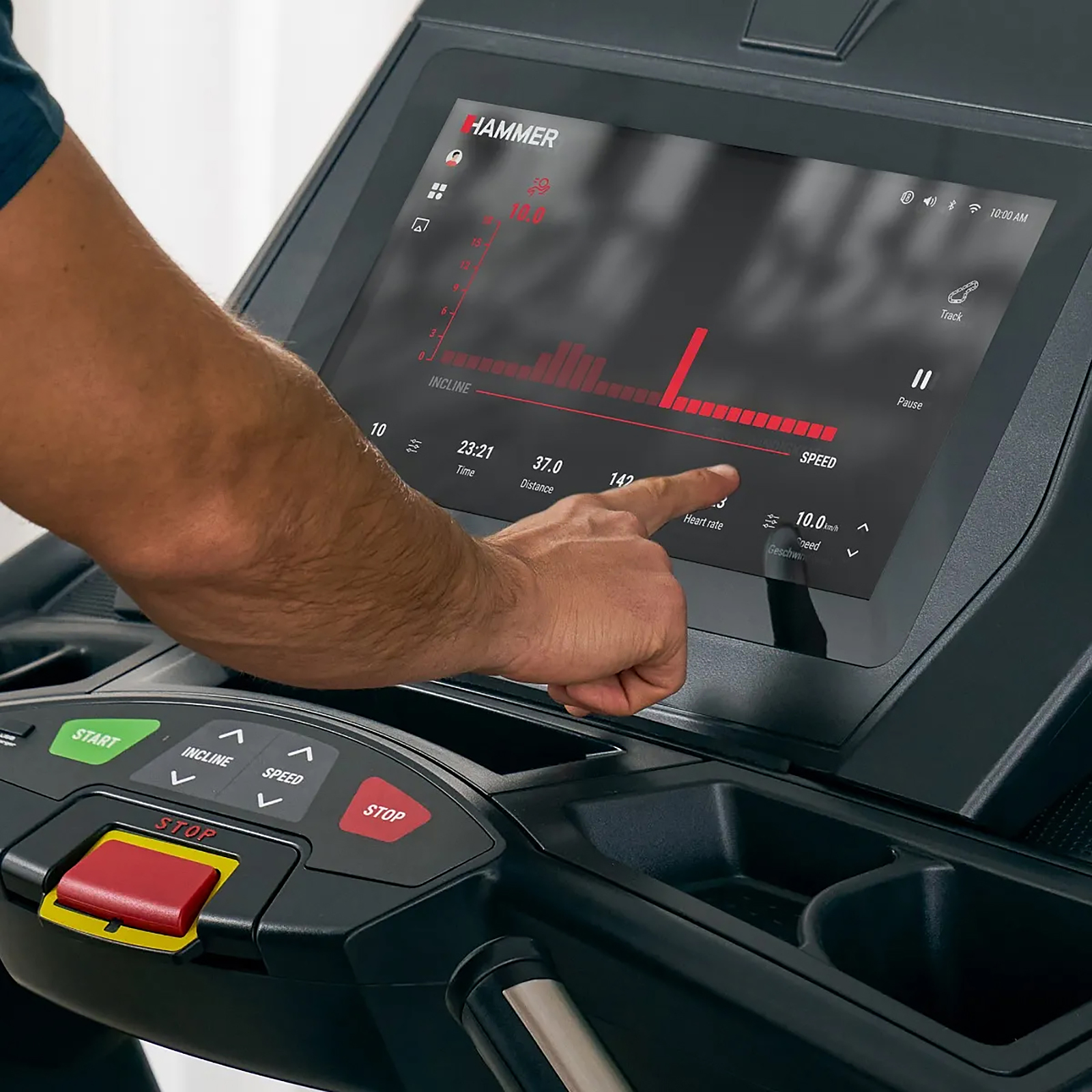 Die Hand einer Person berührt einen Laufbandbildschirm, der Trainingsdaten anzeigt. Das Laufband hat Knöpfe für Geschwindigkeit, Steigung und Stopp.