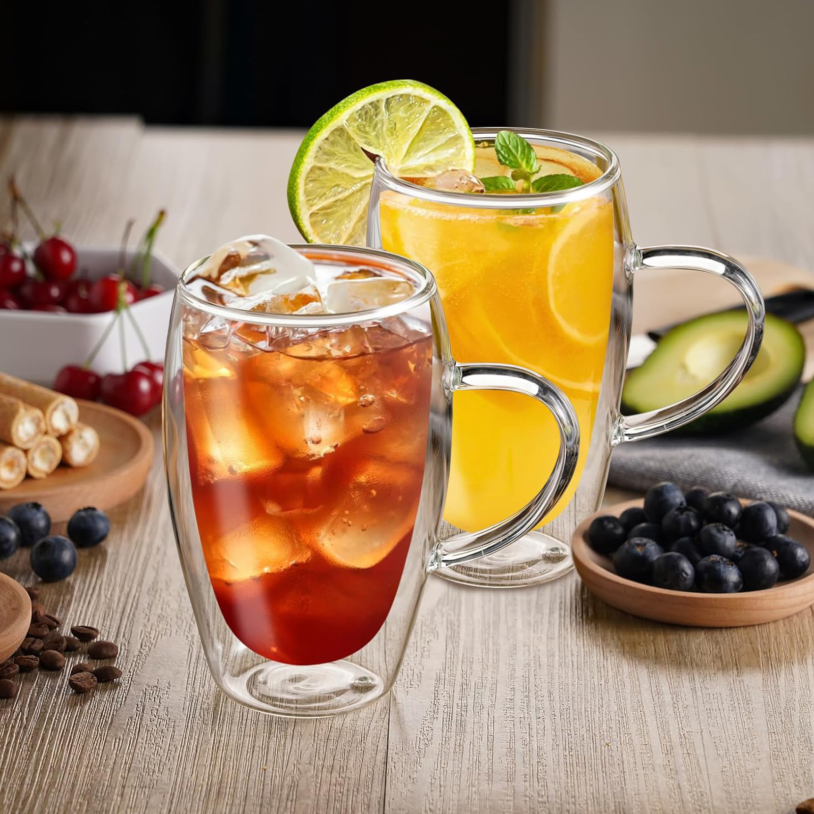 Zwei Glasbecher mit Eisgetränken, einer mit Limette und der andere mit Eis. Kirschen, Blaubeeren und andere Lebensmittel sind sichtbar.