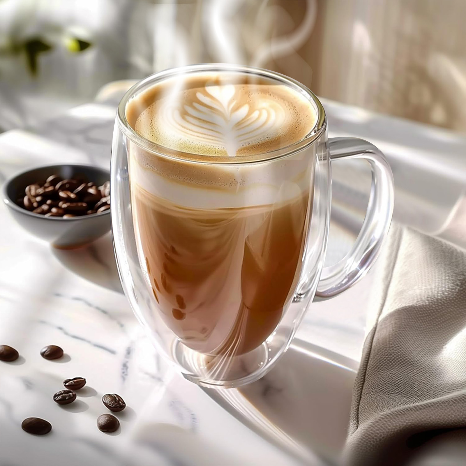 Ein klares Glas mit Kaffee und Milchschaumkunst. Kaffeebohnen und eine Schüssel stehen daneben auf einer weißen Oberfläche.