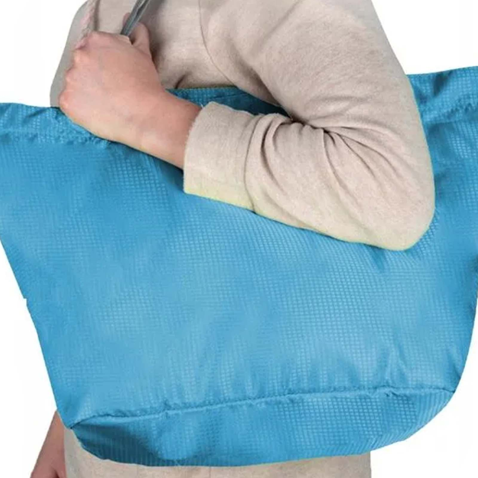 Una persona tiene in mano una grande borsa blu. La borsa è strutturata. La persona indossa una camicia beige a maniche lunghe.