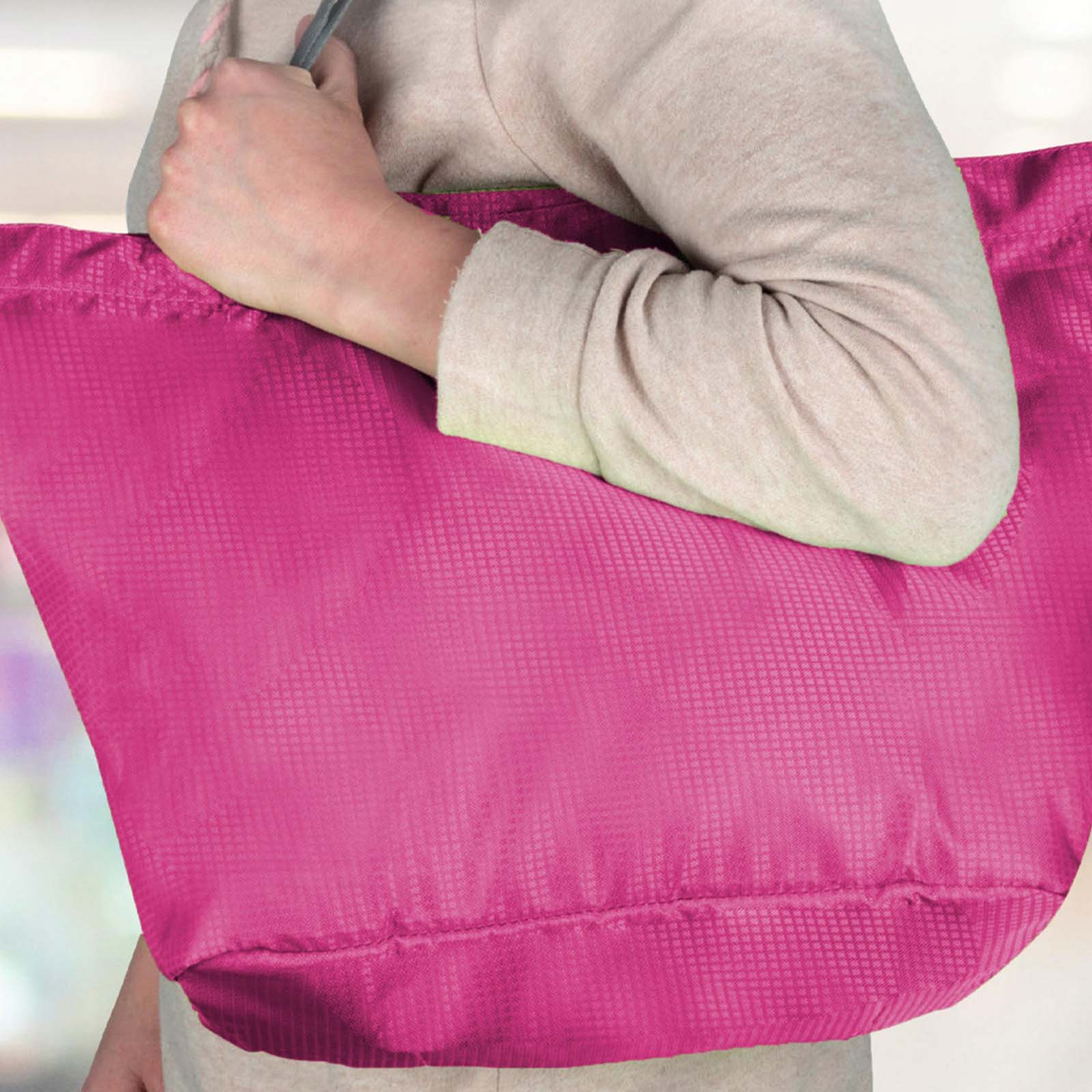 Una persona tiene in mano una grande borsa tote rosa. La borsa è tenuta vicino al petto e il braccio è visibile.