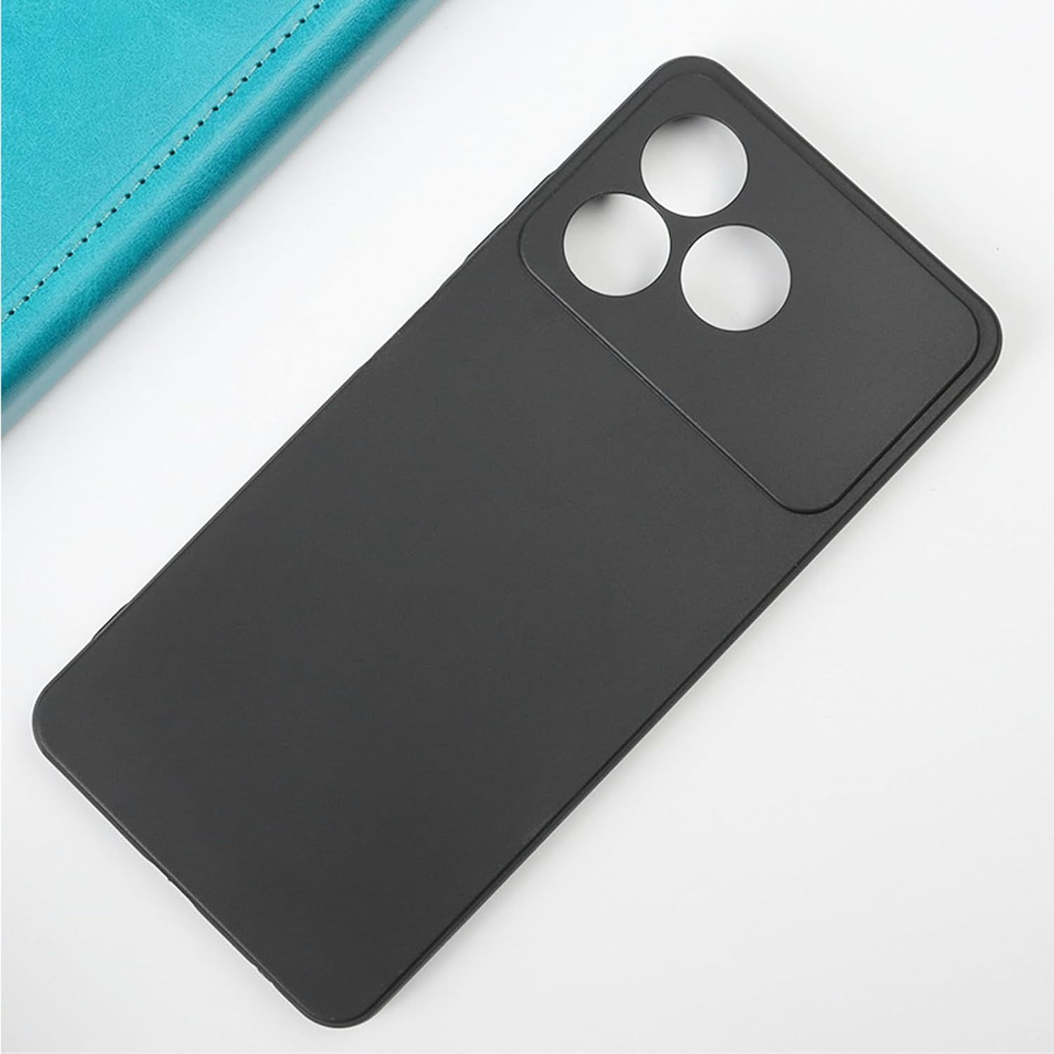 Funda de teléfono negra con tres recortes para la cámara. Un objeto azul en el fondo. La funda está sobre una superficie blanca.