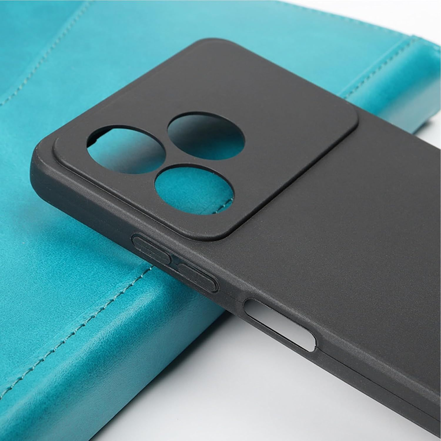 Una funda de teléfono negra sobre un cuaderno de cuero turquesa. La funda tiene recortes para la cámara y botones. El cuaderno tiene bordes cosidos.