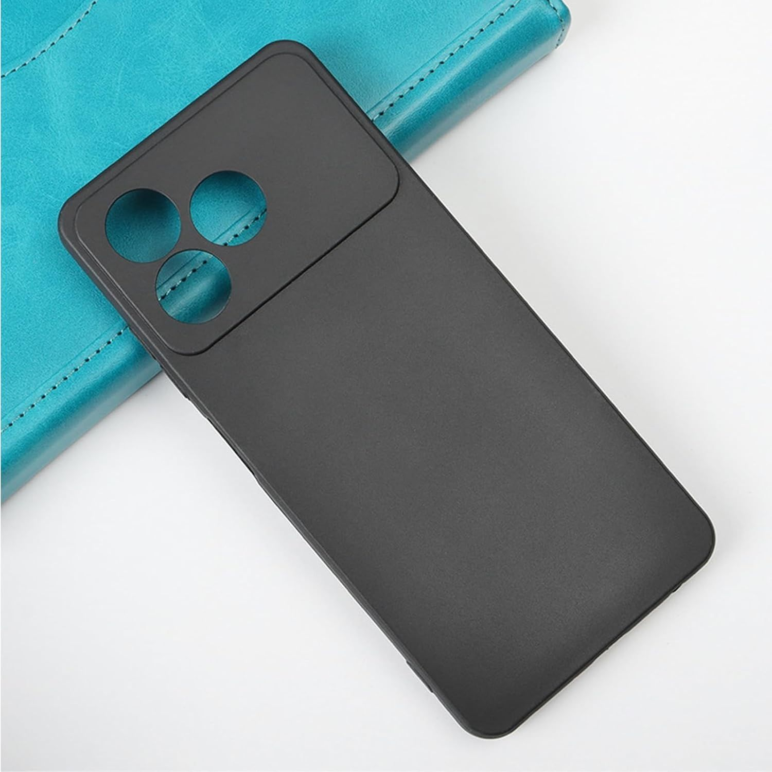 Funda de teléfono negra con recortes para la cámara sobre un cuaderno azul, sobre un fondo blanco. La funda tiene un acabado mate.