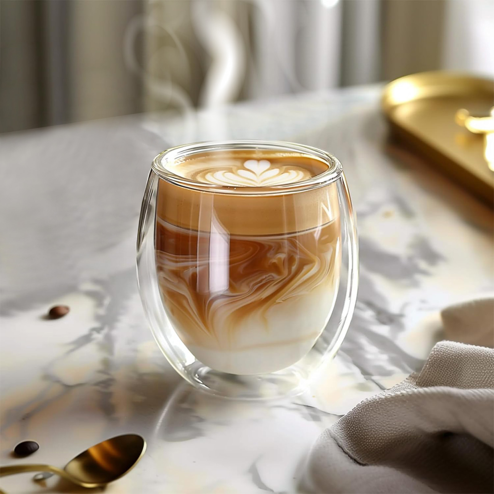 Ein doppelwandiges Glas Latte mit herzförmiger Milchschaumkunst. Dampf steigt auf. Kaffeebohnen und ein goldener Löffel auf Marmoroberfläche.