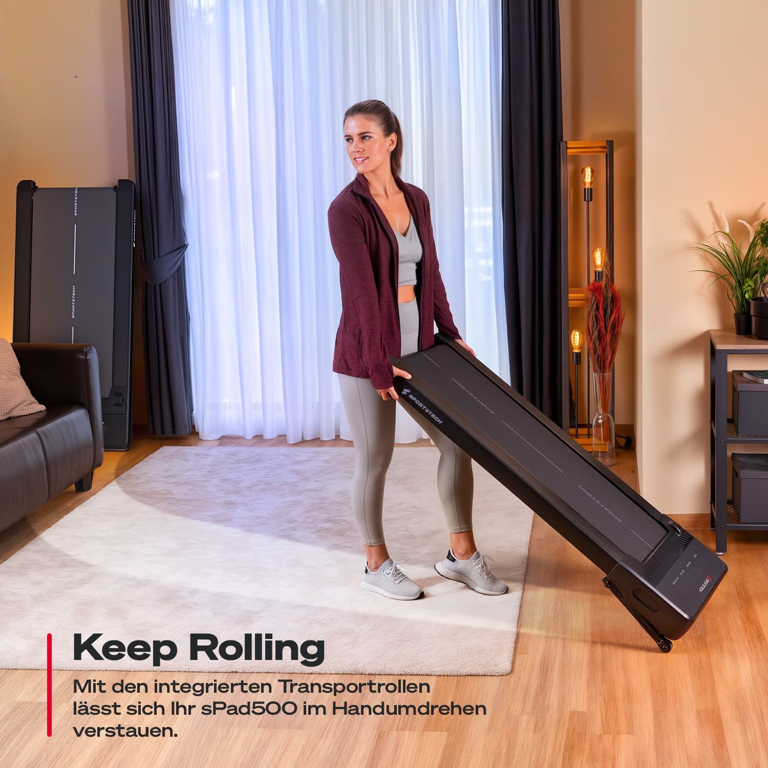 Eine Frau rollt ein schwarzes Laufband. Sie trägt Sportkleidung in einem Wohnzimmer mit weißem Teppich und dunklen Vorhängen.