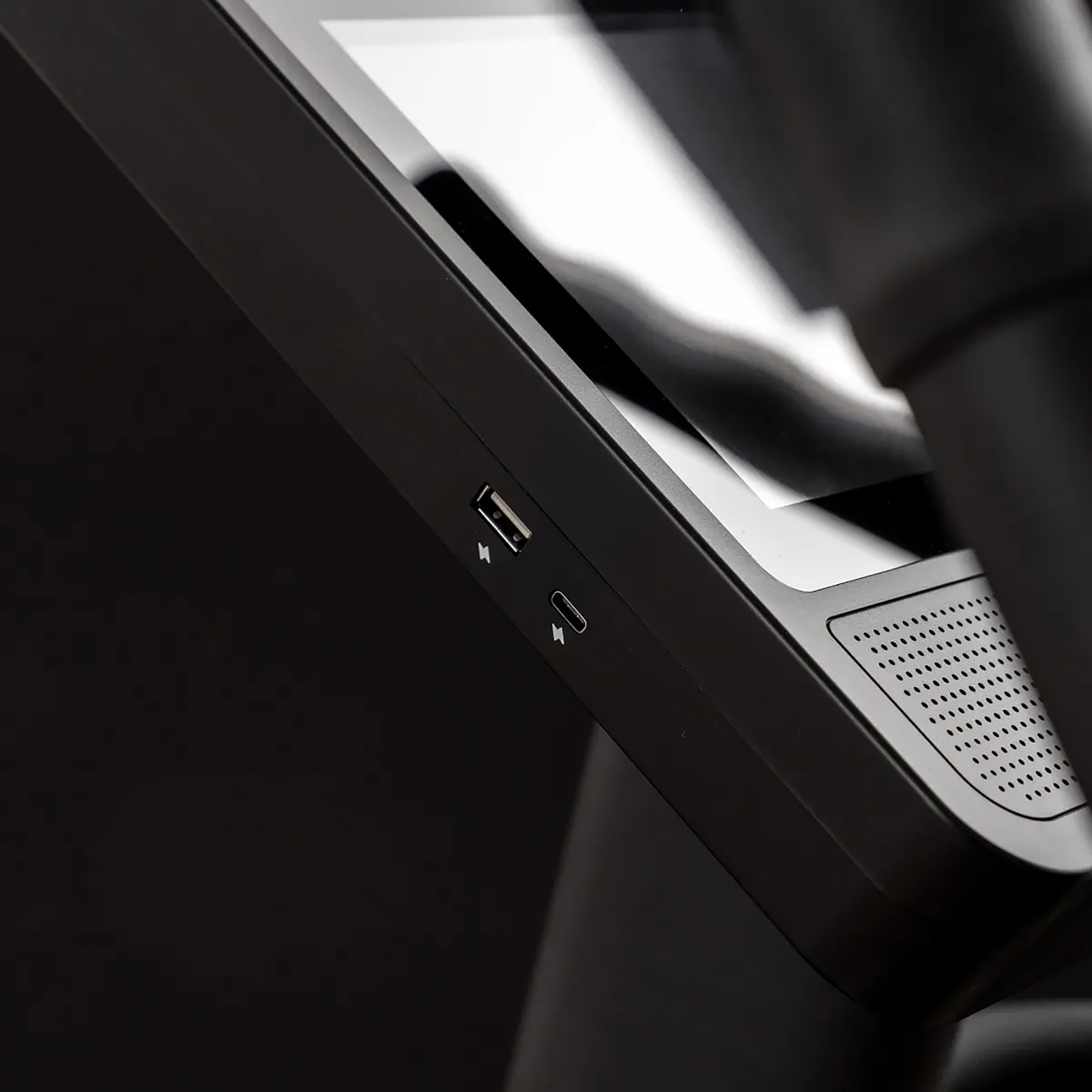 Nahaufnahme einer schwarzen Fitness-Maschinenseite. Enthält USB- und USB-C-Anschlüsse, einen Lautsprecher und einen reflektierenden Bildschirm. Dunkler Hintergrund.