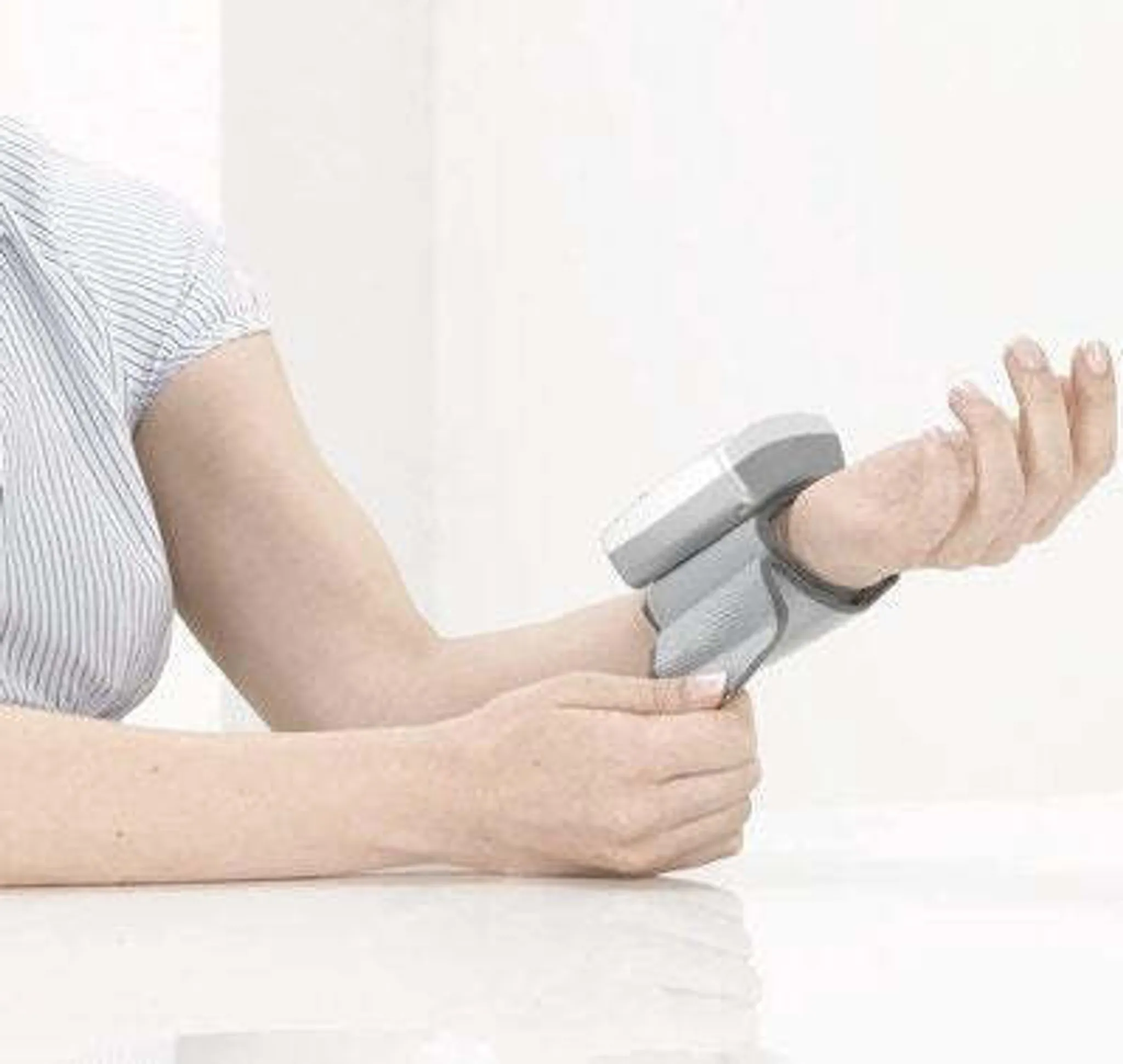 Person trägt ein medizinisches Gerät am Handgelenk. Das Gerät ist grau. Der Arm der Person ist sichtbar. Weißer Hintergrund.
