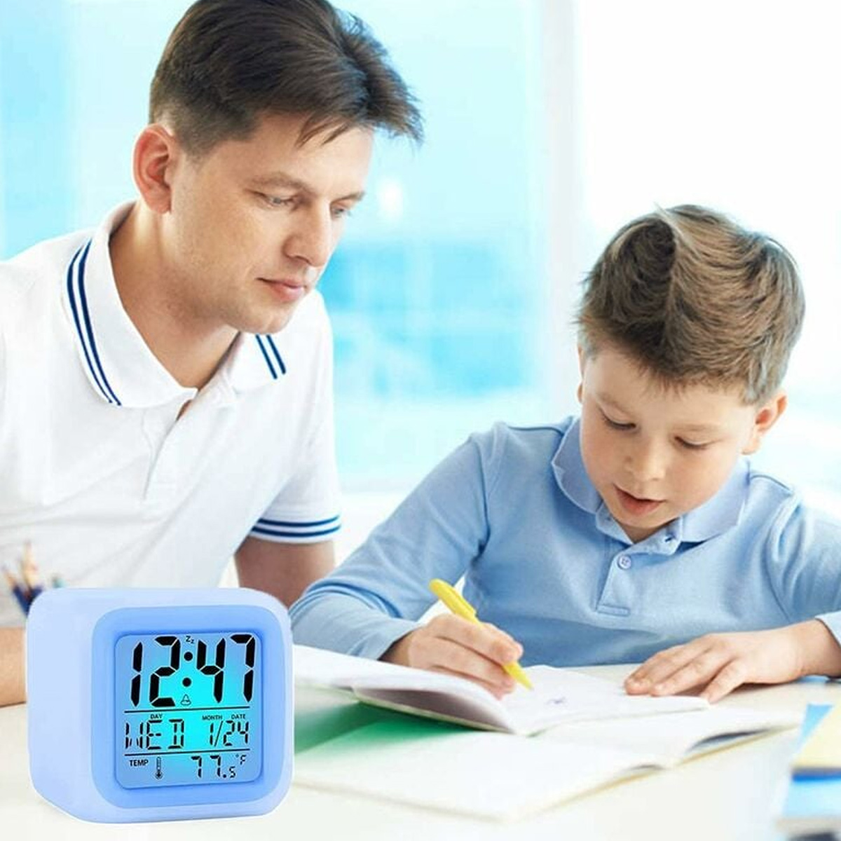 Vater und Sohn in einem Raum. Der Junge schreibt in ein Notizbuch. Eine blaue Uhr zeigt Zeit, Datum und Temperatur.