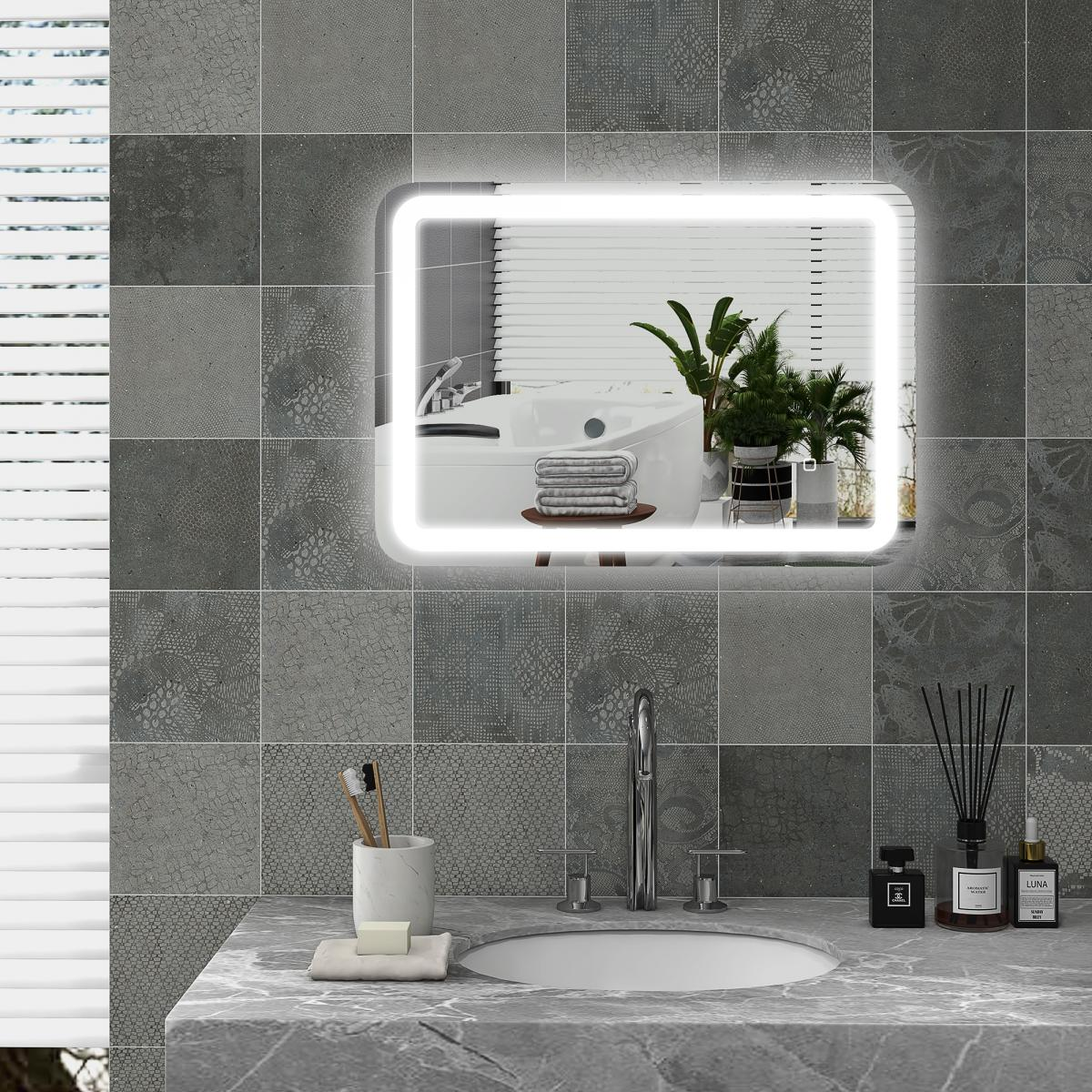 Badezimmer mit beleuchtetem Spiegel, Waschbecken und grauen Fliesen. Der Spiegel reflektiert Badewanne, Pflanzen und Handtücher.
