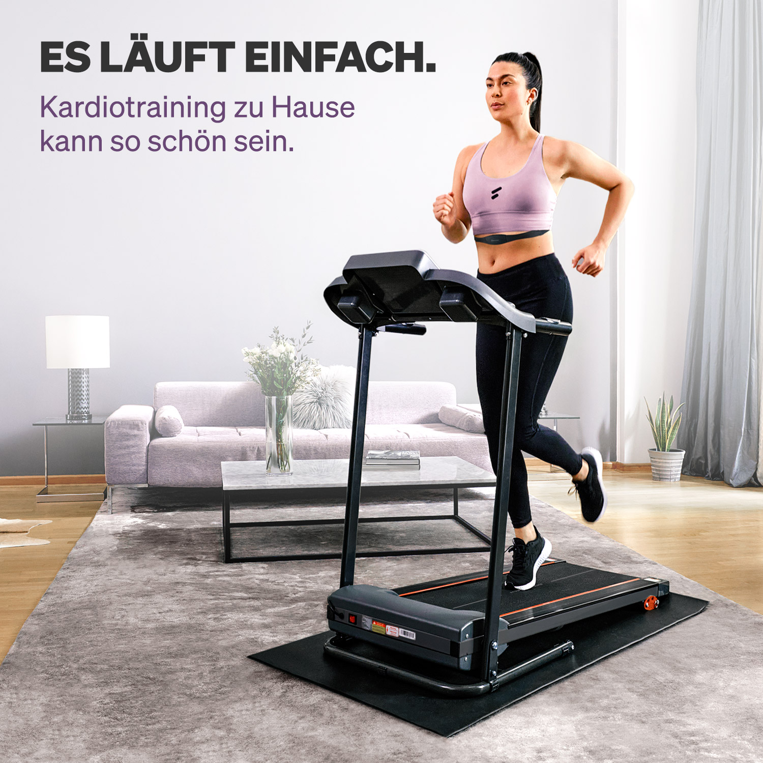 Eine Frau läuft drinnen auf einem Laufband. Sie trägt Trainingskleidung. Im Hintergrund sind eine Couch und ein Couchtisch zu sehen.