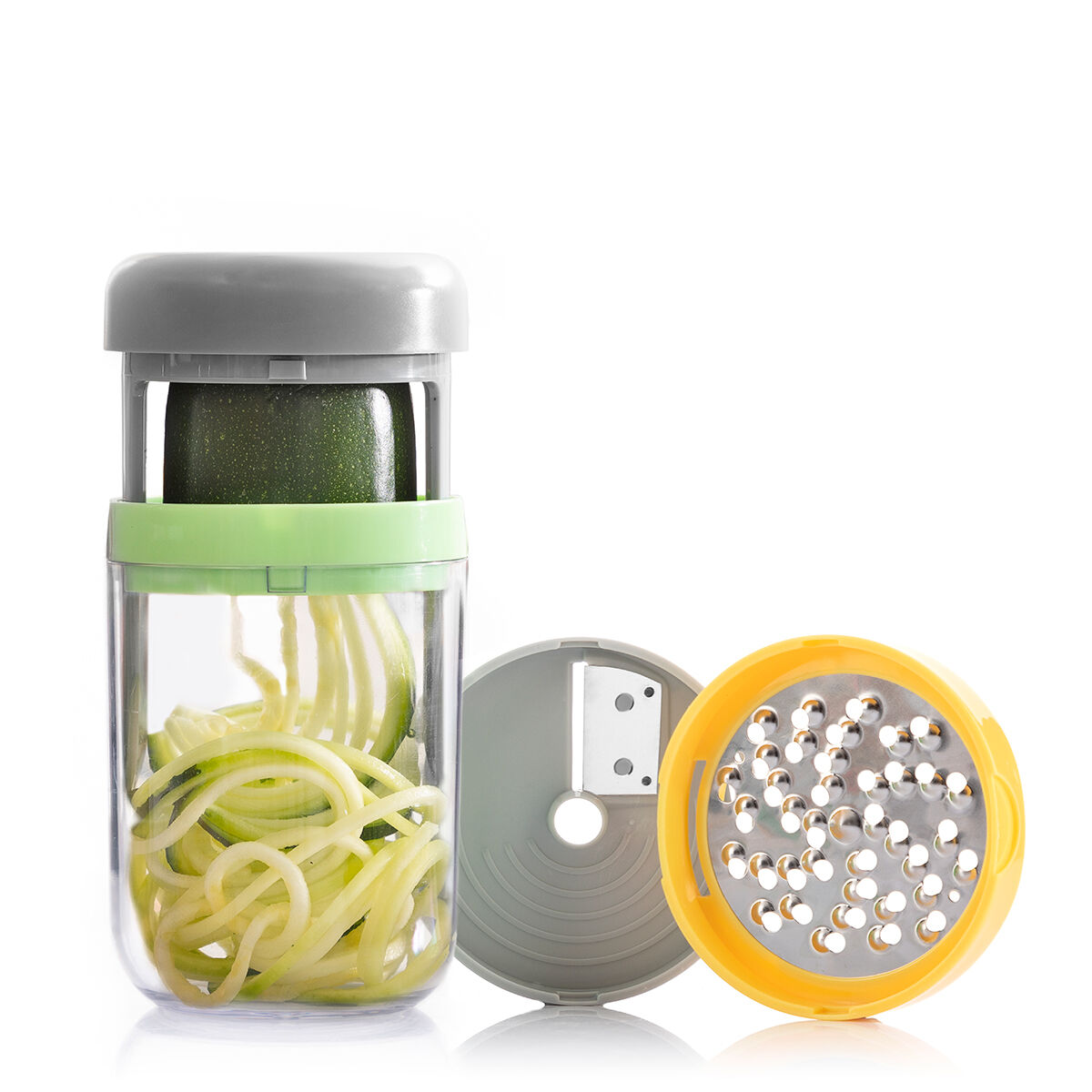Uno spiralizzatore di verdure con zucchine all'interno e spirali nel contenitore. Una grattugia e un coperchio sono accanto su sfondo bianco.