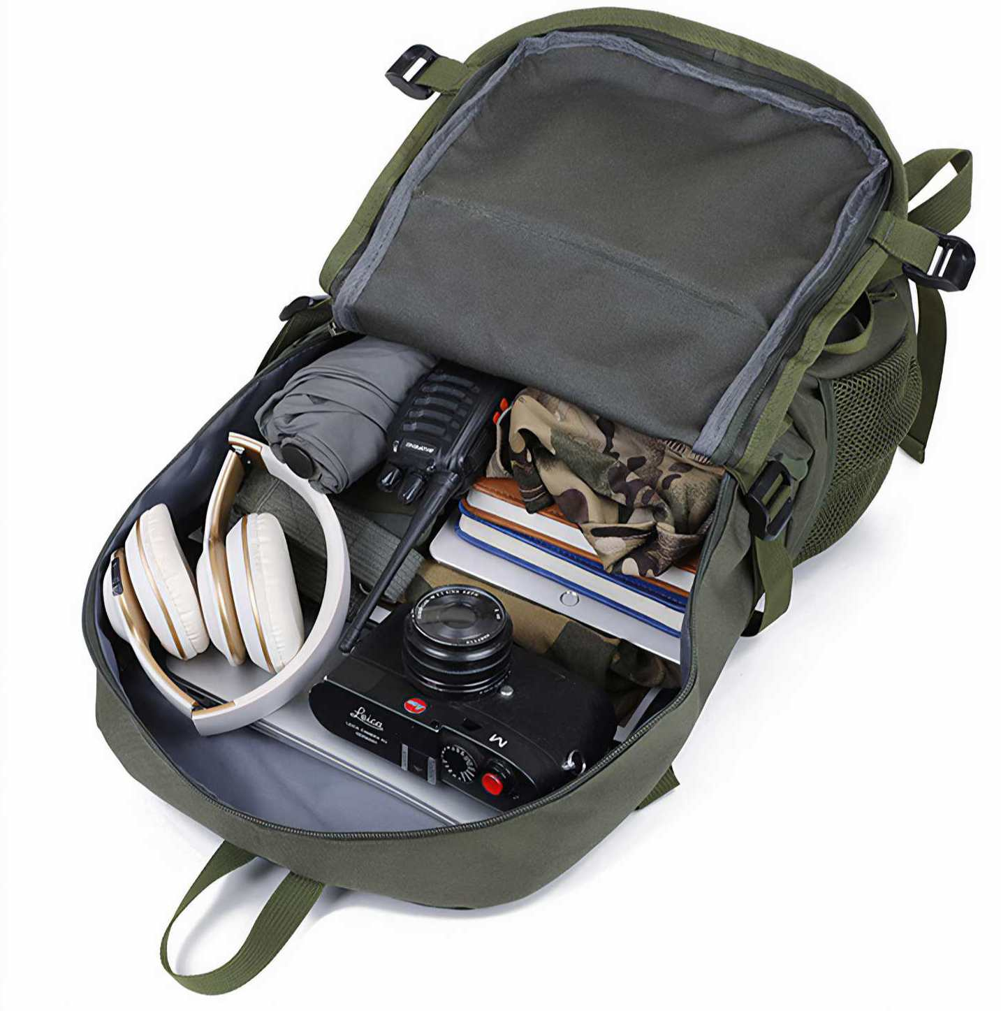 Offener grüner Rucksack mit Gegenständen gefüllt: Kopfhörer, Kamera, Bücher, Funkgerät, Regenschirm und Tarnstoff. Isoliert vor weißem Hintergrund.
