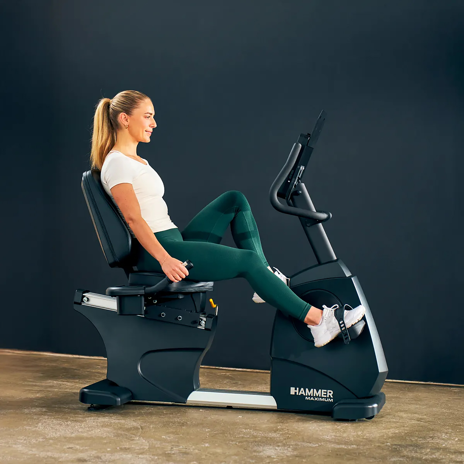 Eine Frau auf einem Heimtrainer. Sie trägt ein weißes Hemd, grüne Leggings und weiße Schuhe. Das Fahrrad ist schwarz.