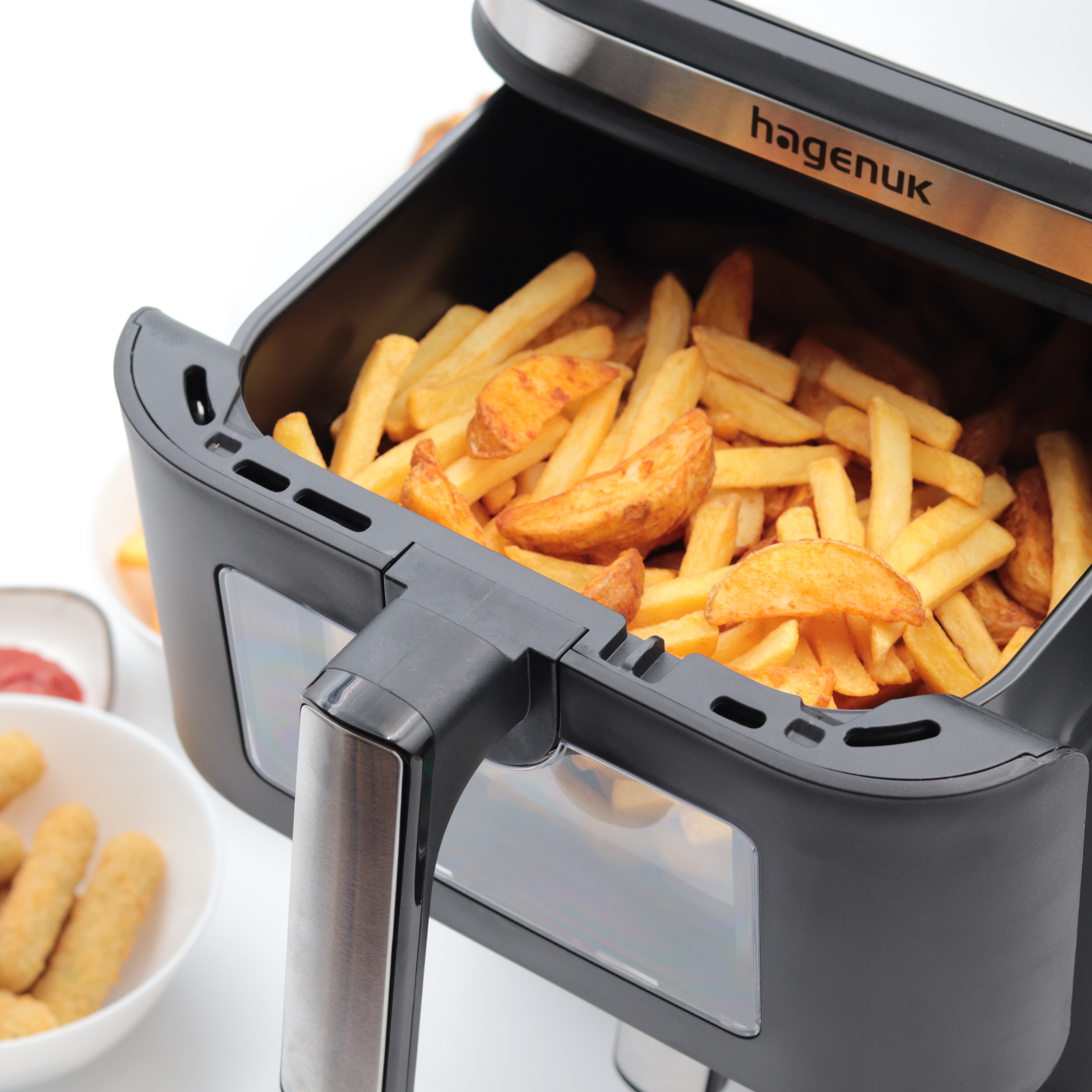 Heißluftfritteuse mit Pommes Frites. Andere Gerichte wie Chicken Nuggets und Saucen sind sichtbar.