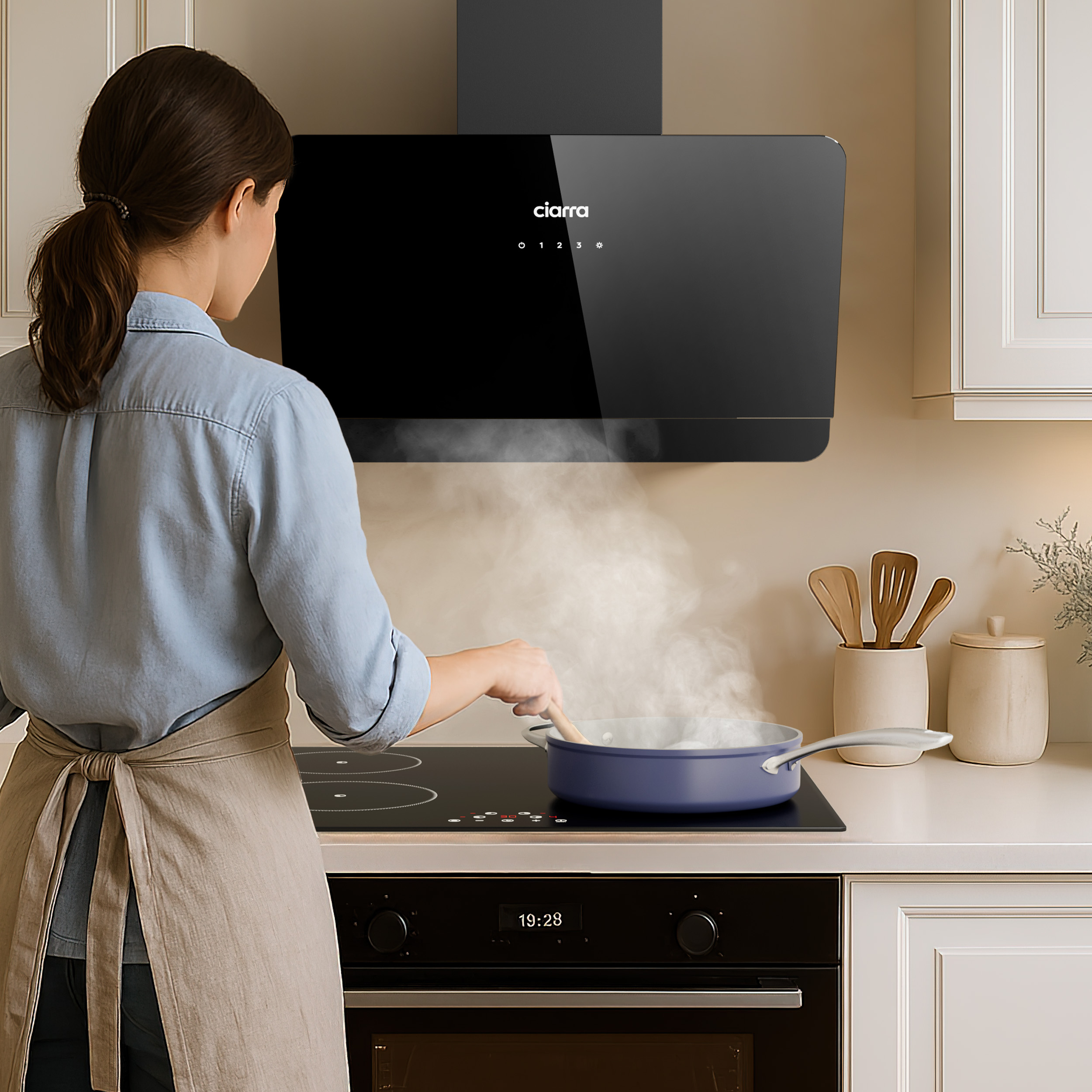Vrouw kookt in keuken. Zwarte afzuigkap, blauwe pan op kookplaat. Stoom komt op. Beige schort.