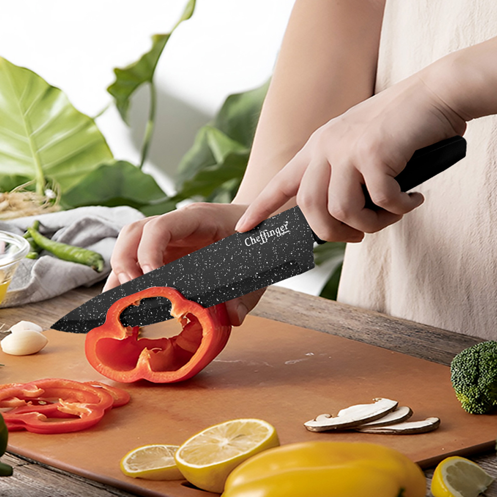 Eine Person schneidet eine rote Paprika mit einem schwarzen Messer auf einem Schneidebrett. Auf dem Brett liegen weiteres Gemüse und Zitronen.