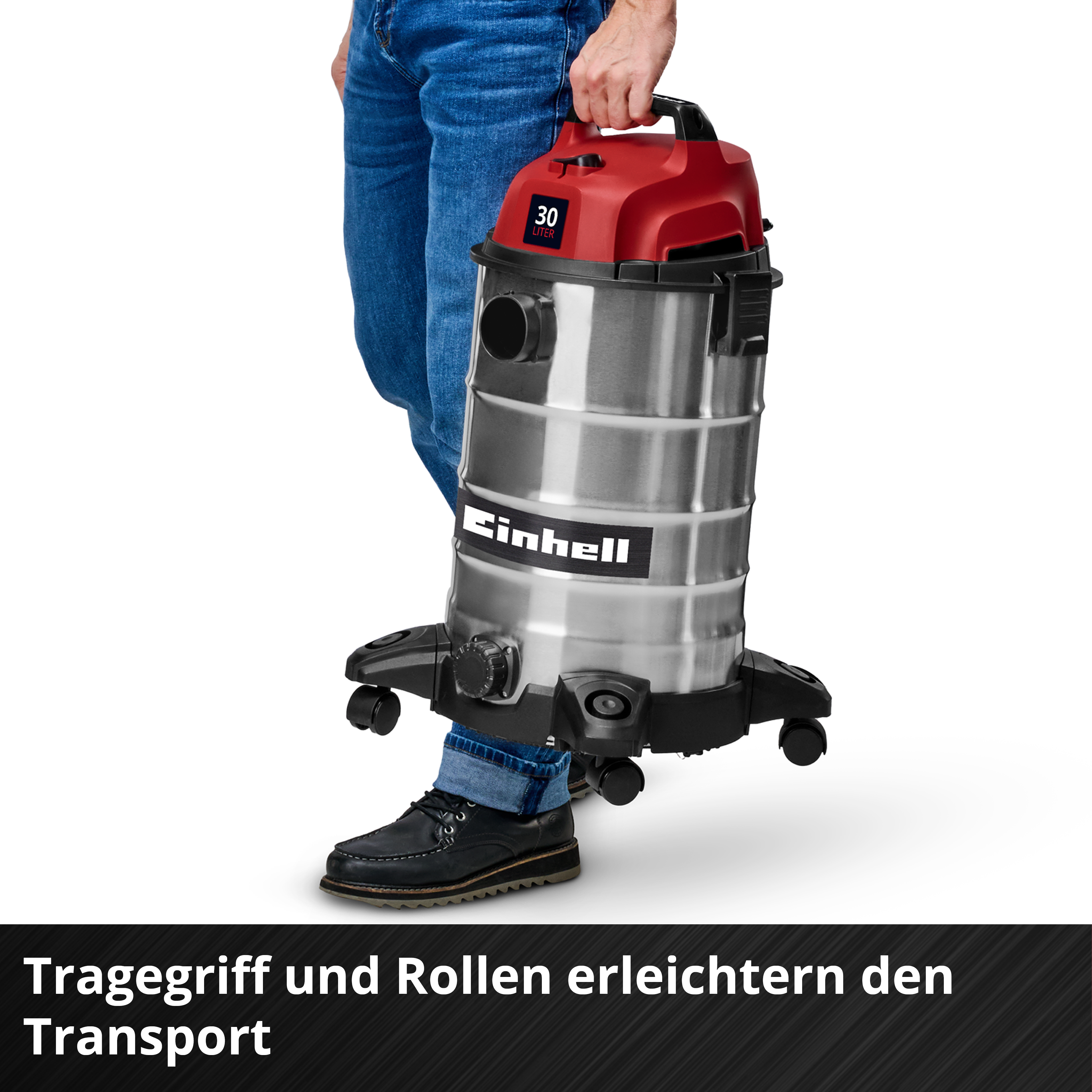 Un homme tient un aspirateur. Il est argenté avec un dessus rouge et des roues noires. La poignée est en haut.