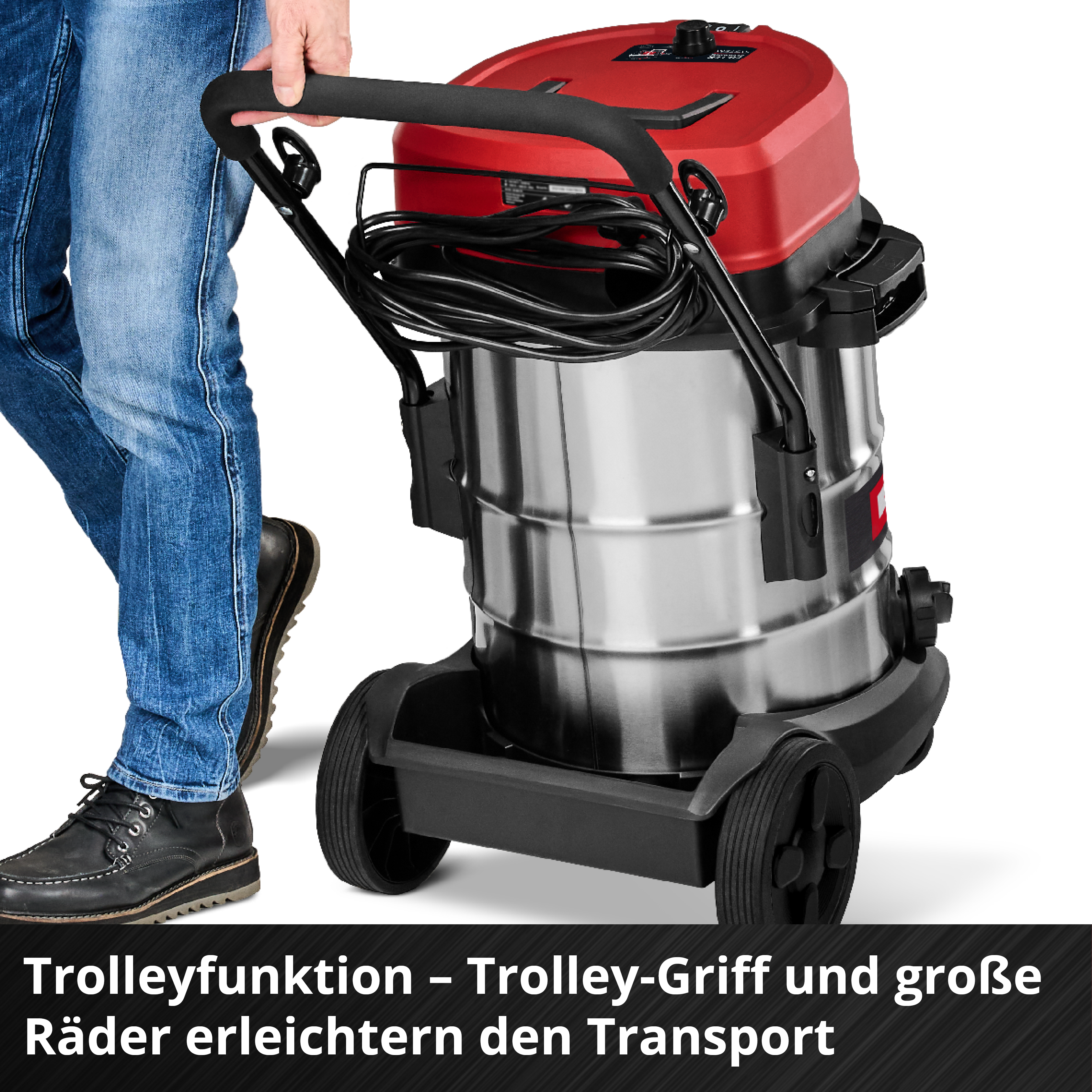 Eine Person hält einen Staubsauger. Der Staubsauger ist rot und silber. Die Person trägt blaue Jeans und schwarze Schuhe.
