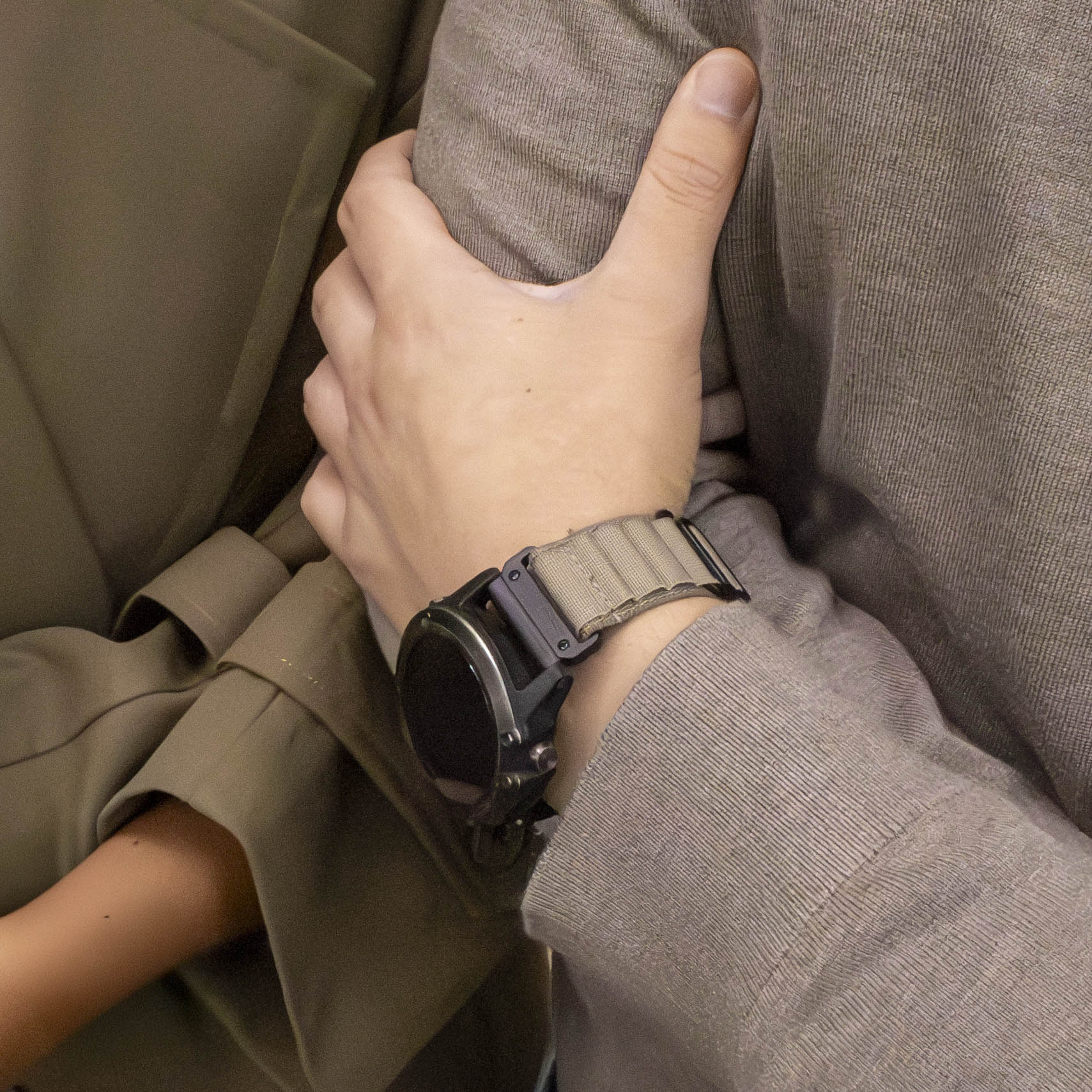 Die Hand einer Person mit einer Uhr am Handgelenk. Sie trägt ein beiges Uhrenarmband. Die Person trägt ein tanfarbenes Hemd.