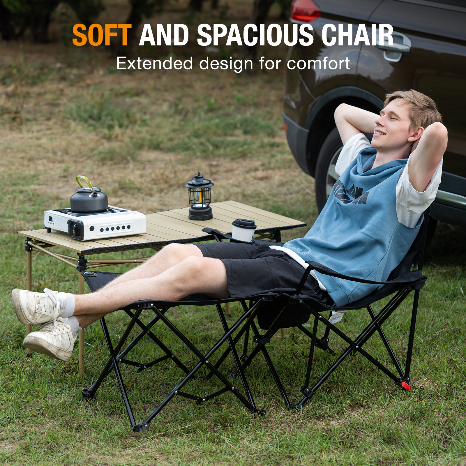 A man relaxes in a camping chair with his hands behind his head. A table with a stove, lamp, and coffee cup is nearby.
