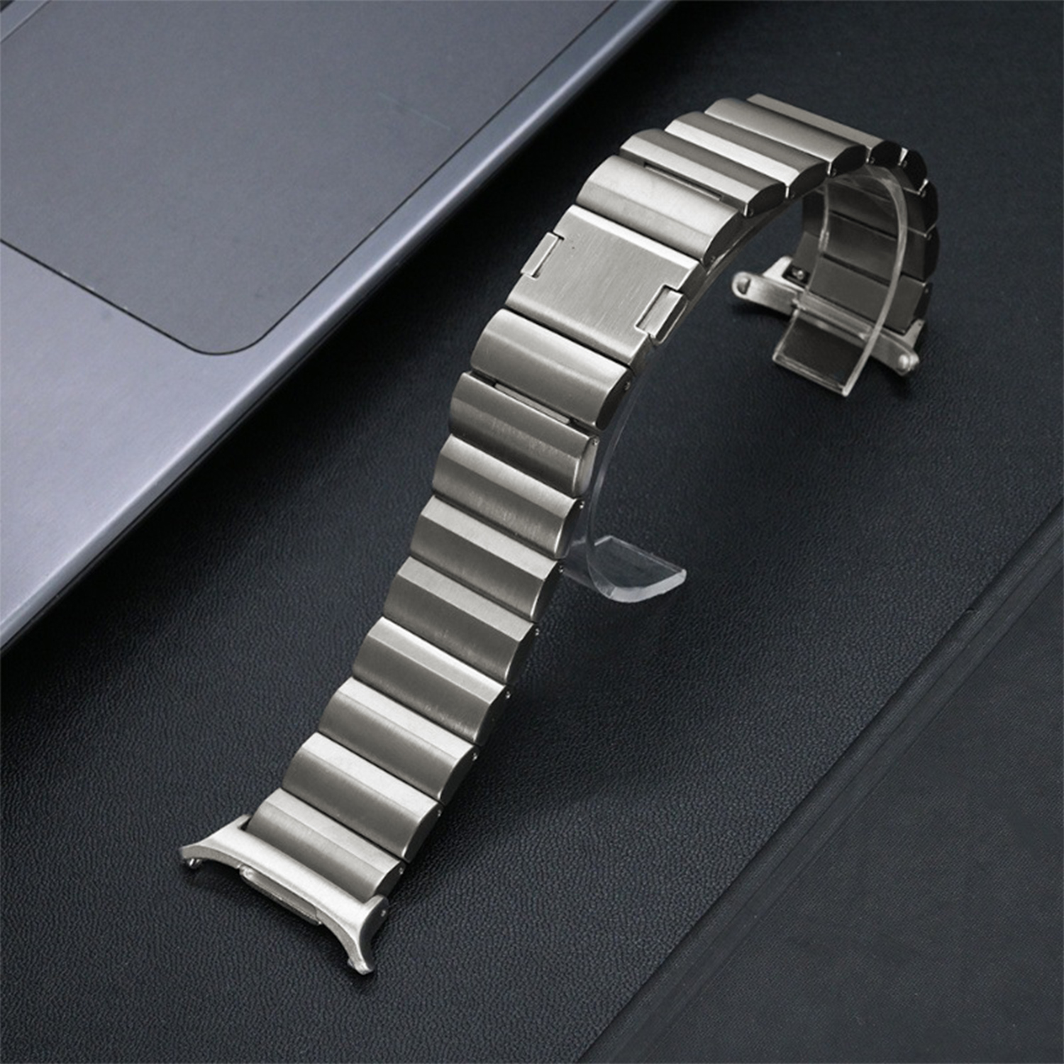 Ein silbernes Uhrenarmband wird auf einer schwarzen Oberfläche gezeigt. Das Armband ist gebogen und besteht aus rechteckigen Metallgliedern.