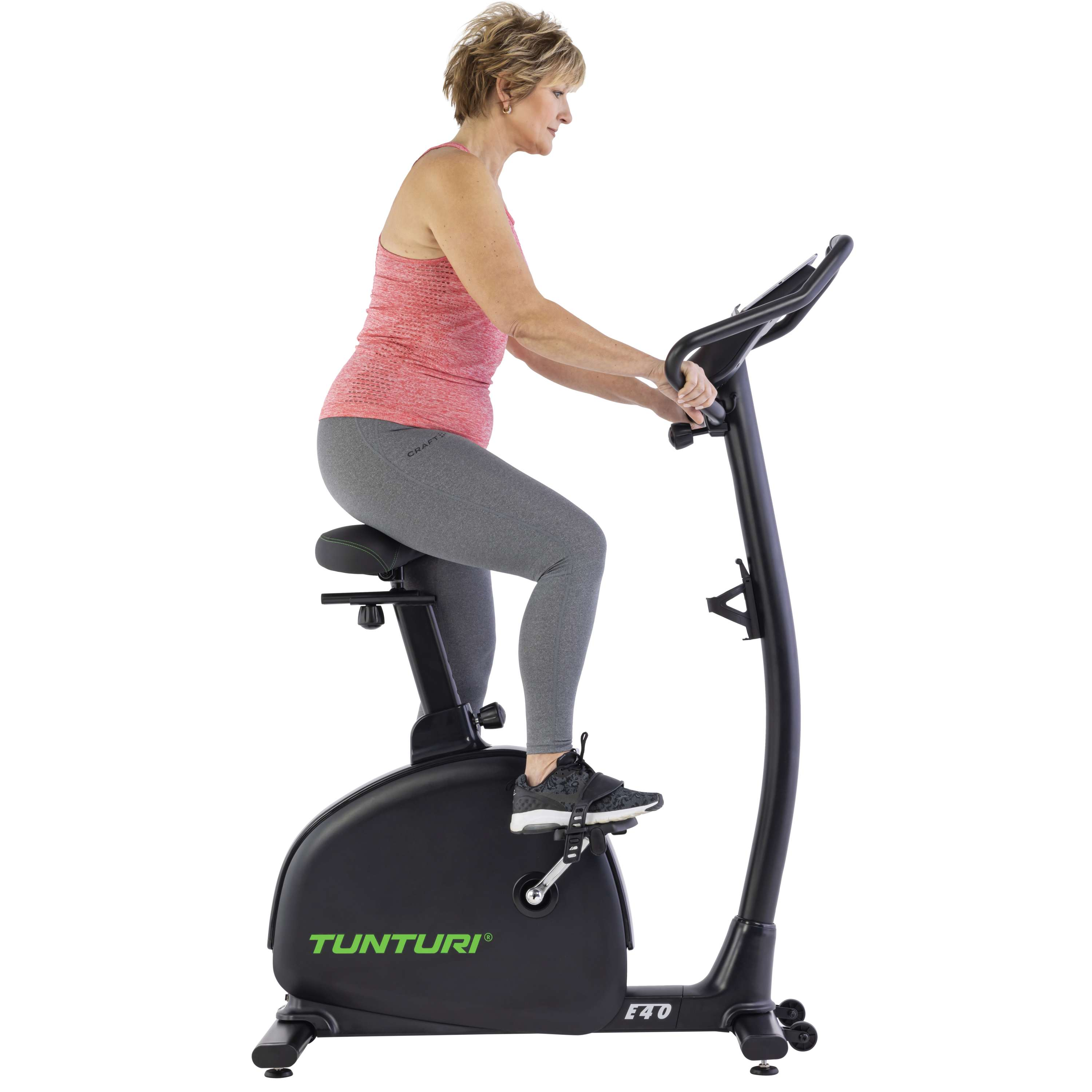 A woman in workout clothes is using a black stationary bike. The bike has the brand name Tunturi. The background is white.